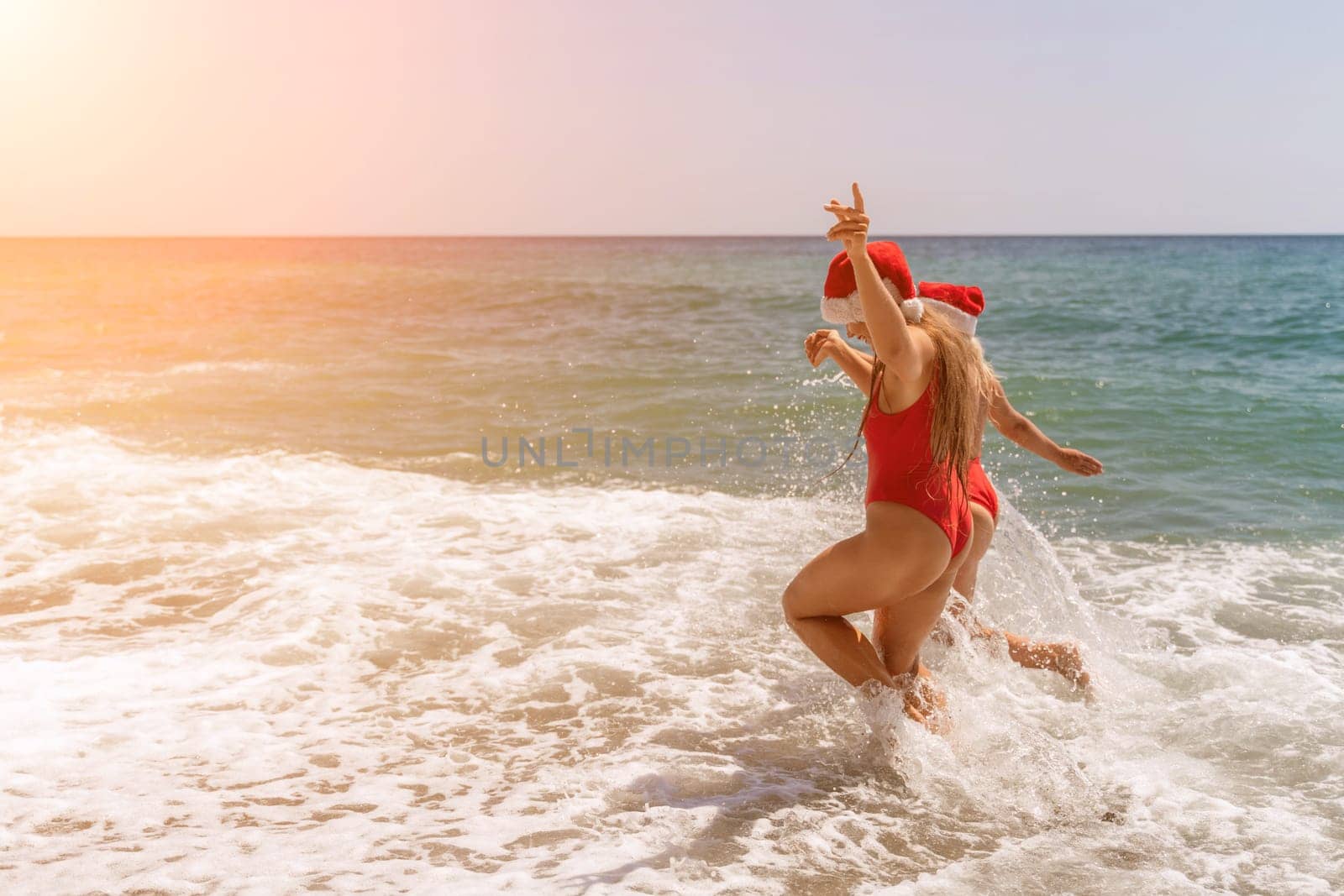 Women in Santa Claus hats run into the sea dressed in red swimsuits. Celebrating the New Year in a hot country by Matiunina