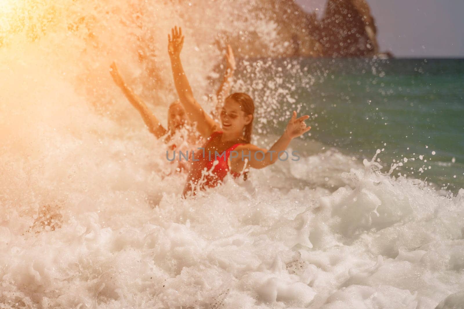 Women ocean play. Seaside, beach daytime, enjoying beach fun. Two women in red swimsuits enjoying themselves in the ocean waves and raising their hands up