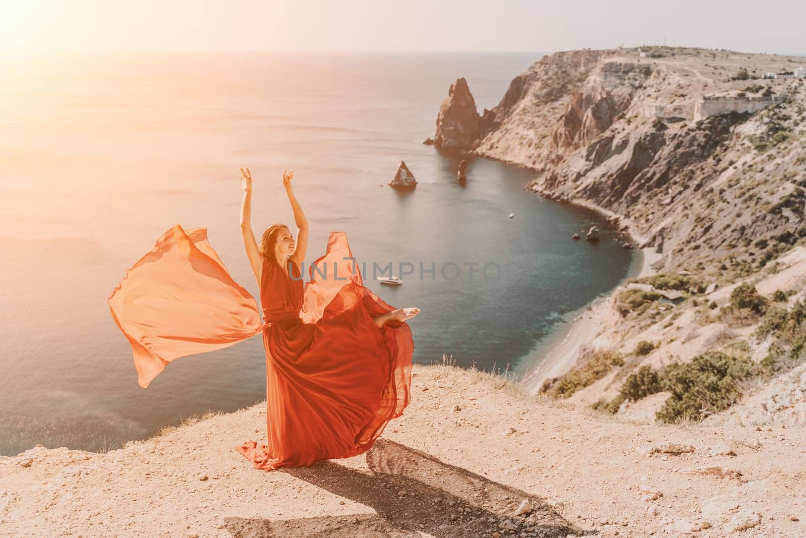 Woman red dress sea. Female dancer in a long red dress posing on a beach with rocks on sunny day. Girl on the nature on blue sky background