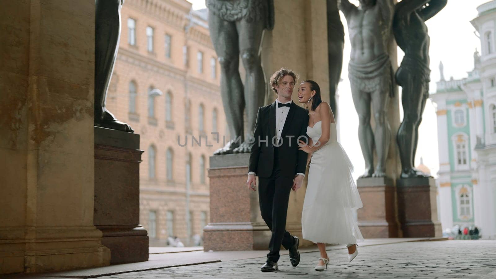 Beautiful newlyweds walking along European street. Action. Happy newlyweds are walking around city in wedding dresses. Newlyweds are walking in Europe.