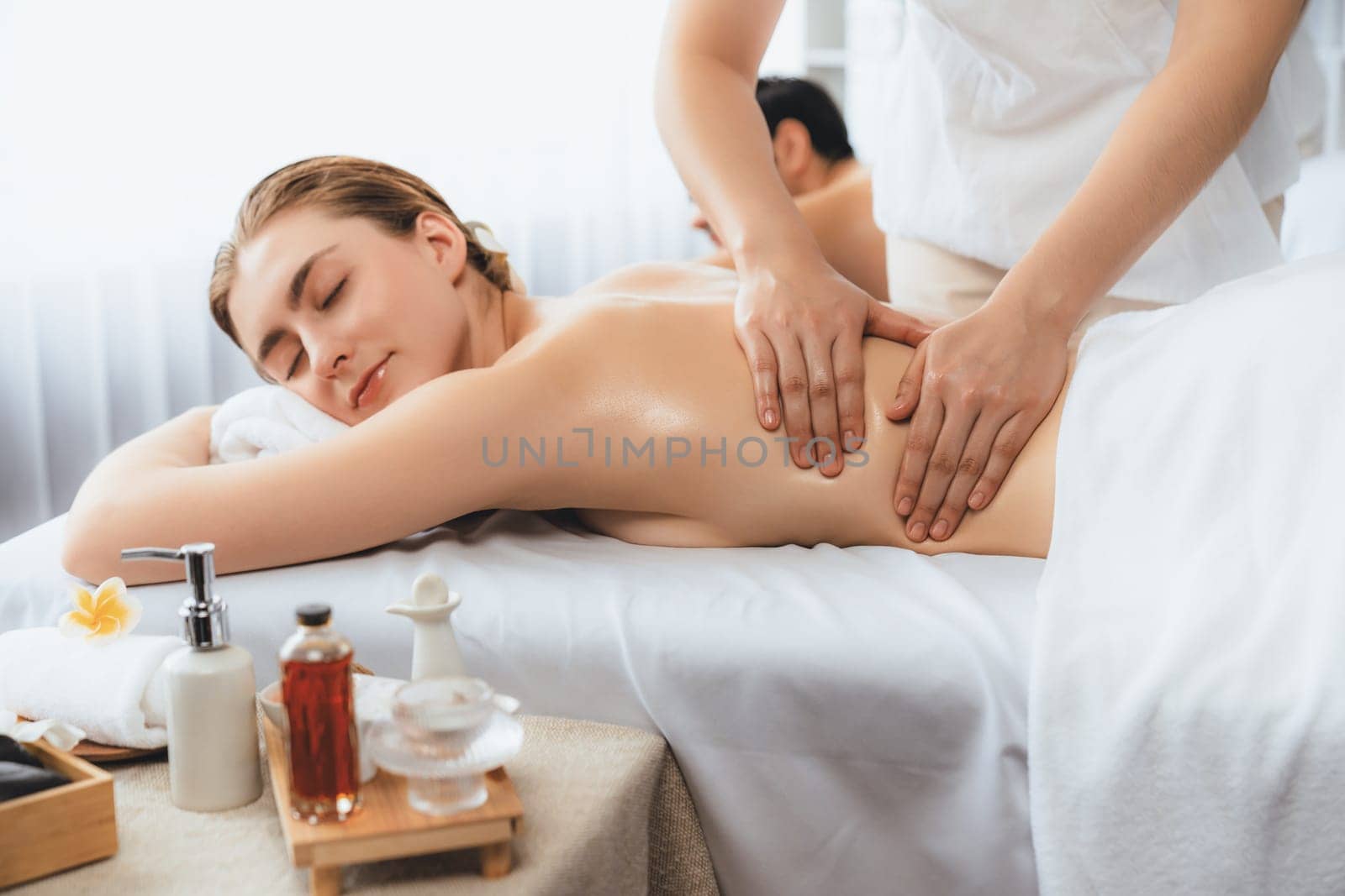 Caucasian couple customer enjoying relaxing anti-stress spa massage and pampering with beauty skin recreation leisure in day light ambient salon spa at luxury resort or hotel. Quiescent