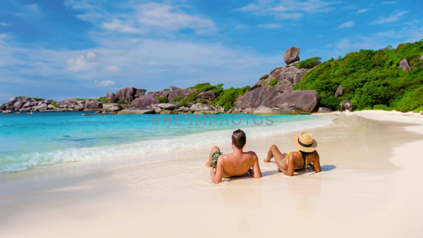A couple of Asian women and white men relaxing on the beach in the sun at the Similan Islands in Thailand Phannga. couple visit the Similan Islands on a boat trip during vacation