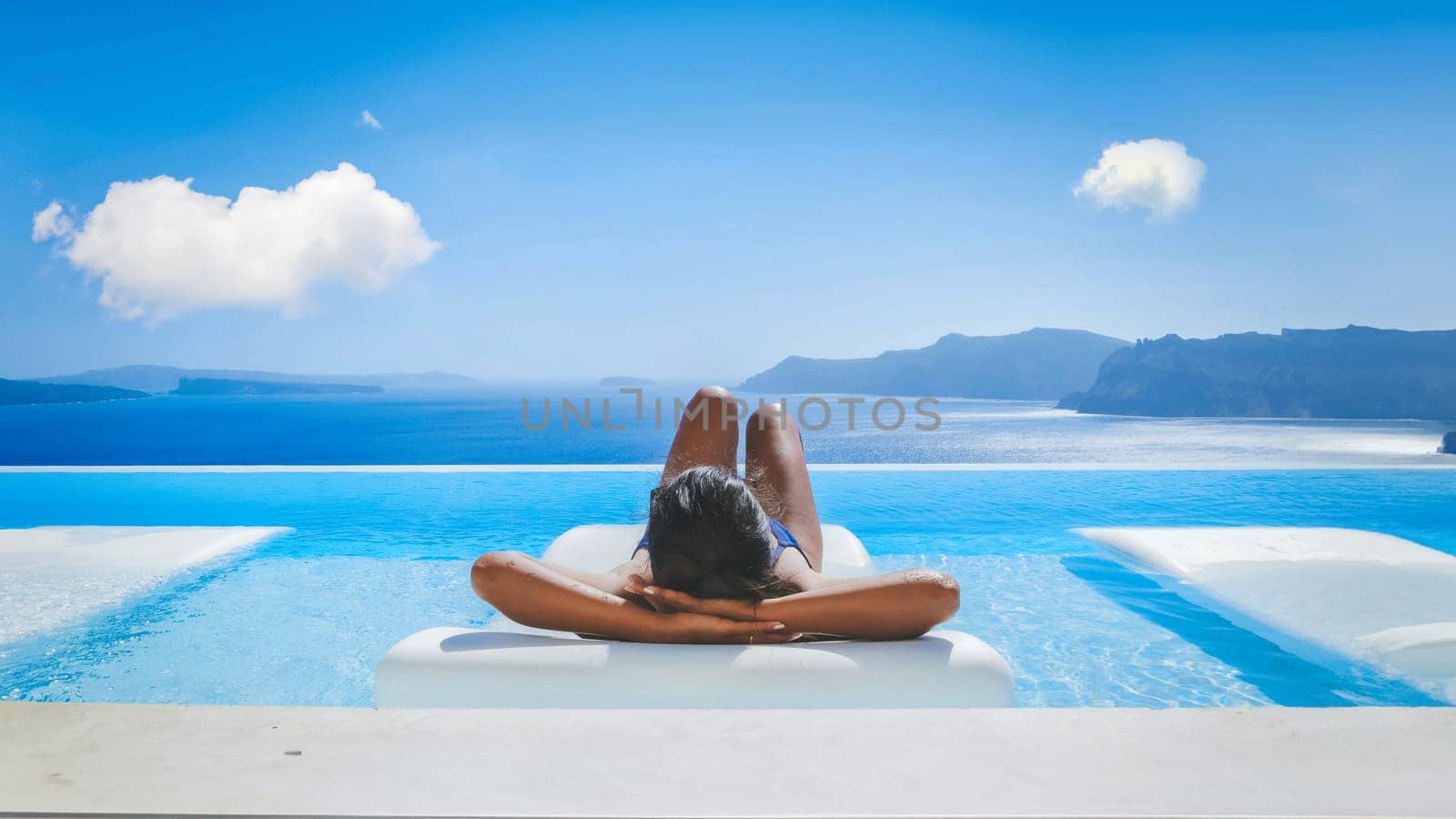 Young Asian women on vacation at Santorini relaxing in a swimming pool looking out over the Caldera ocean of Santorini, Oia Greece, Greek Island Aegean Cyclades during summer in Europe