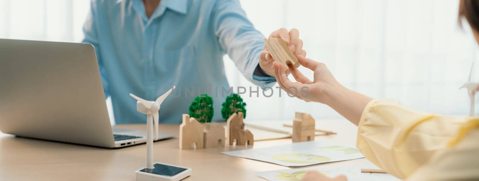 Two business people talking about eco city at green business meeting on meeting table with windmill represented renewable energy, wooden house block and tree model represent green city. Delineation.