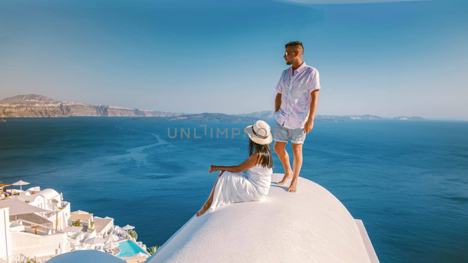 Santorini Greece, a young couple on luxury vacation at the Island Santorini watching the sunrise by the blue dome church and whitewashed village Oia Santorini, Asian women and caucasian men on holiday