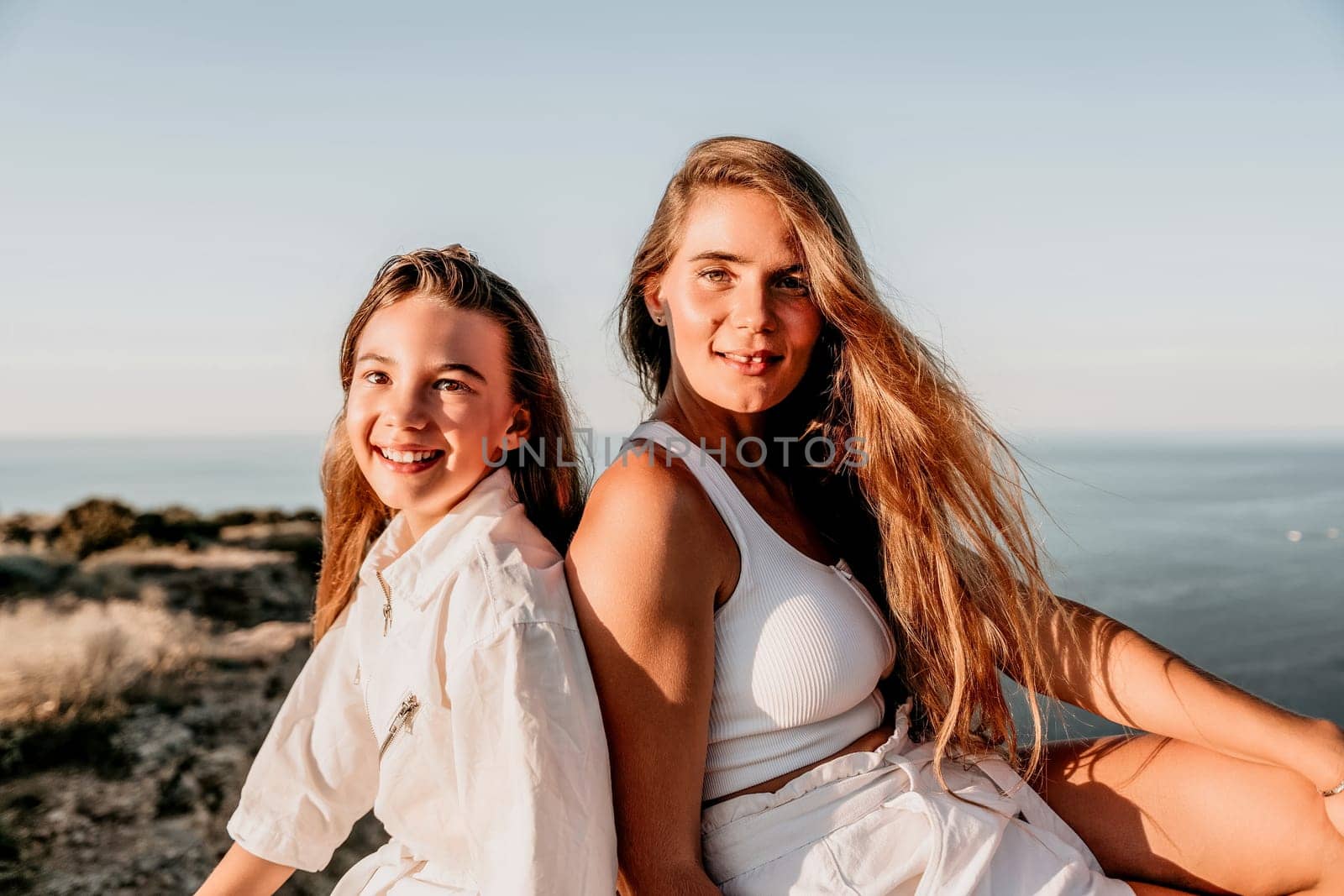 Close up portrait of mom and her teenage daughter hugging and smiling together over sunset sea view. Beautiful woman relaxing with her child.