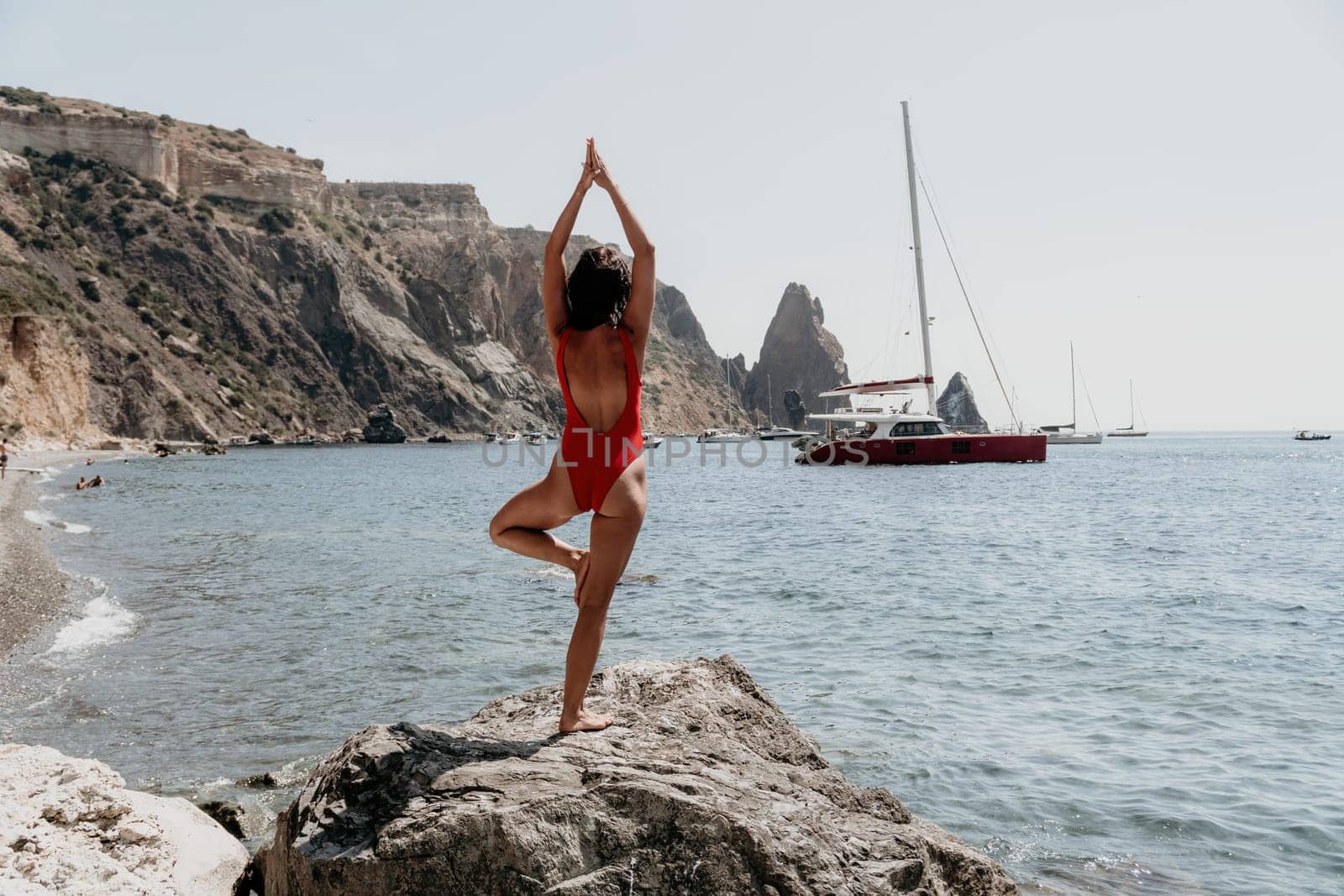 Woman travel portrait. Happy woman with long hair looking at camera and smiling. Close up portrait cute woman in a red bikini posing on a volcanic rock high above the sea by panophotograph