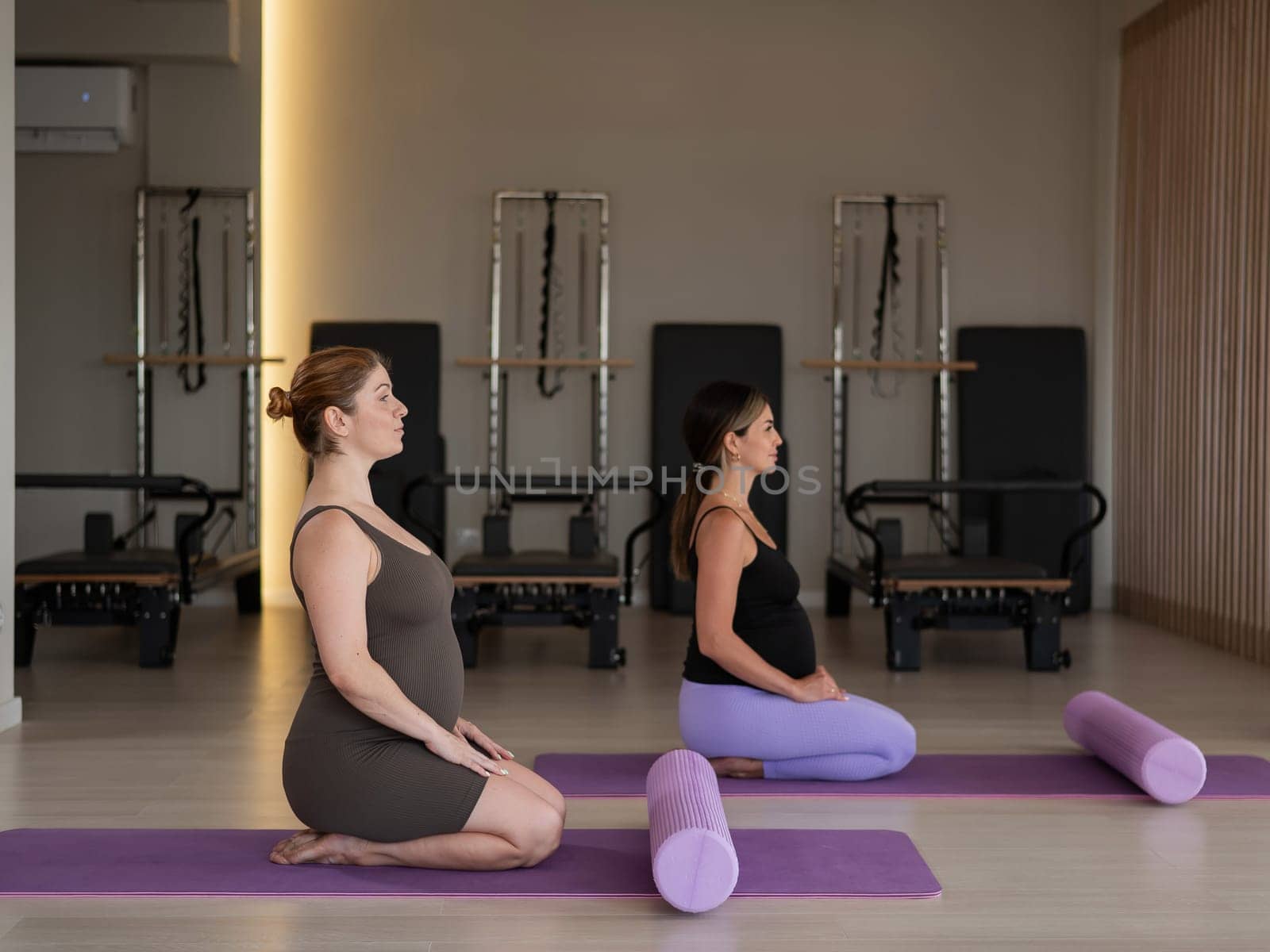 Two pregnant women are sitting on a yoga mat. Prenatal yoga