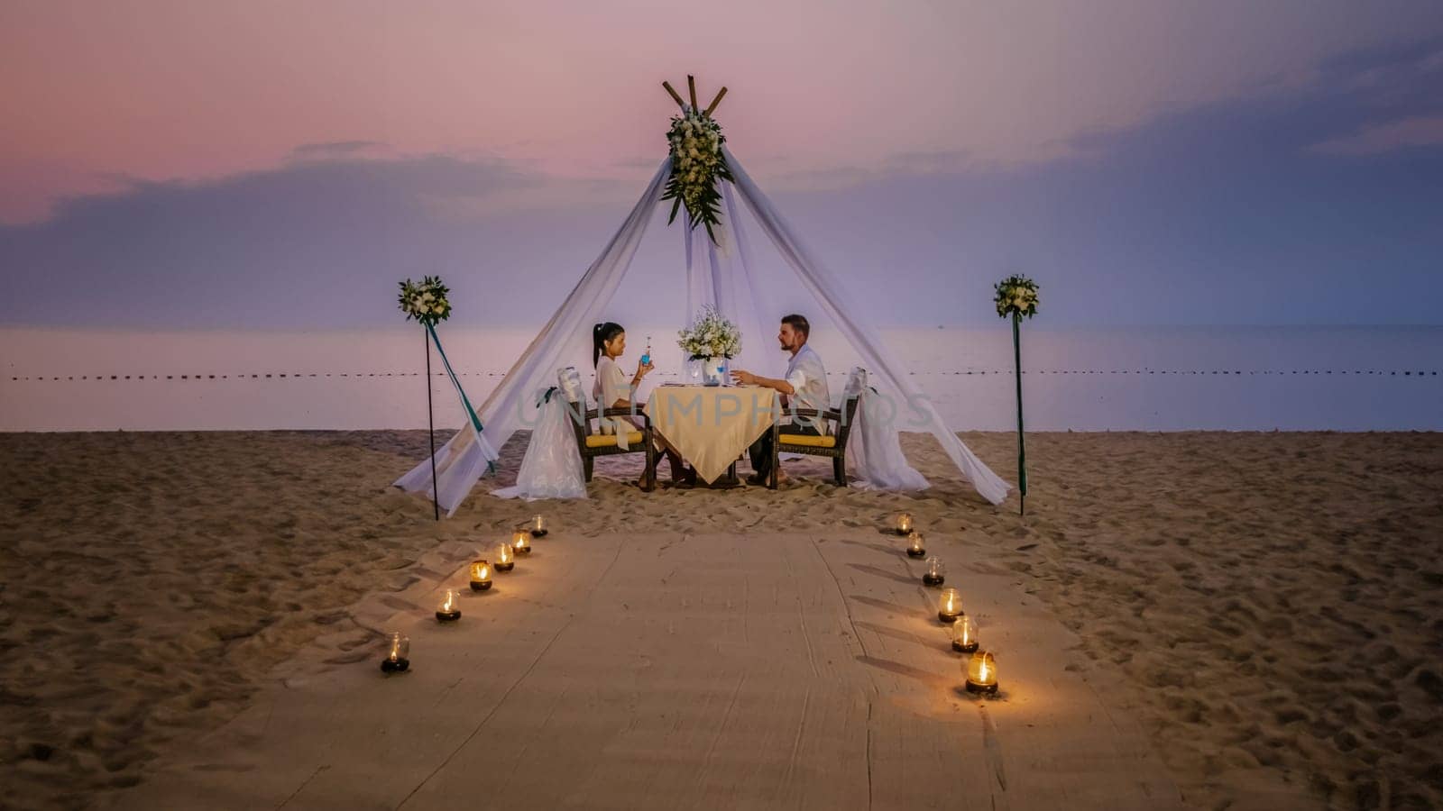 Romantic dinner on the beach, honeymoon dinner on the beach during sunset Thailand, Valentine setting Asia, a couple of men and woman having a romantic dinner by candlelight on the beach in Thailand