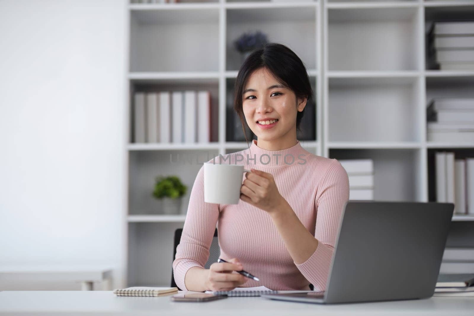 Young Asian woman uses laptop to complete financial transactions, financial planning and investments through online banking. by wichayada