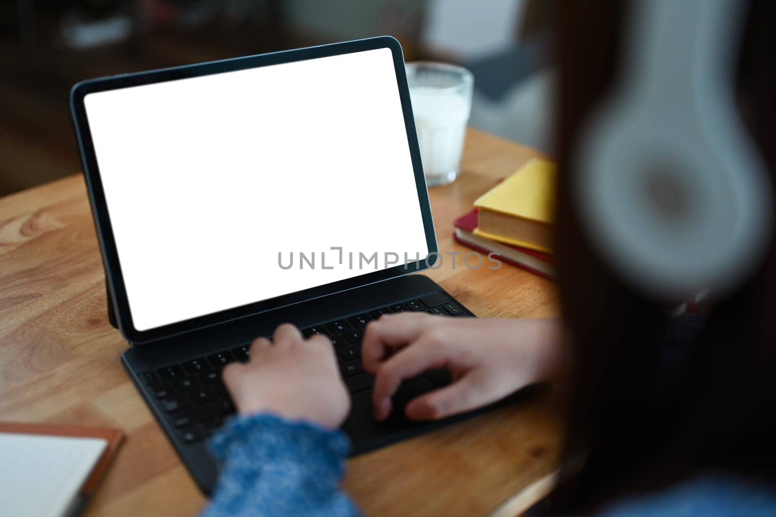 Closeup child girl hands typing on keyboard of digital tablet while doing homework at dinning table.