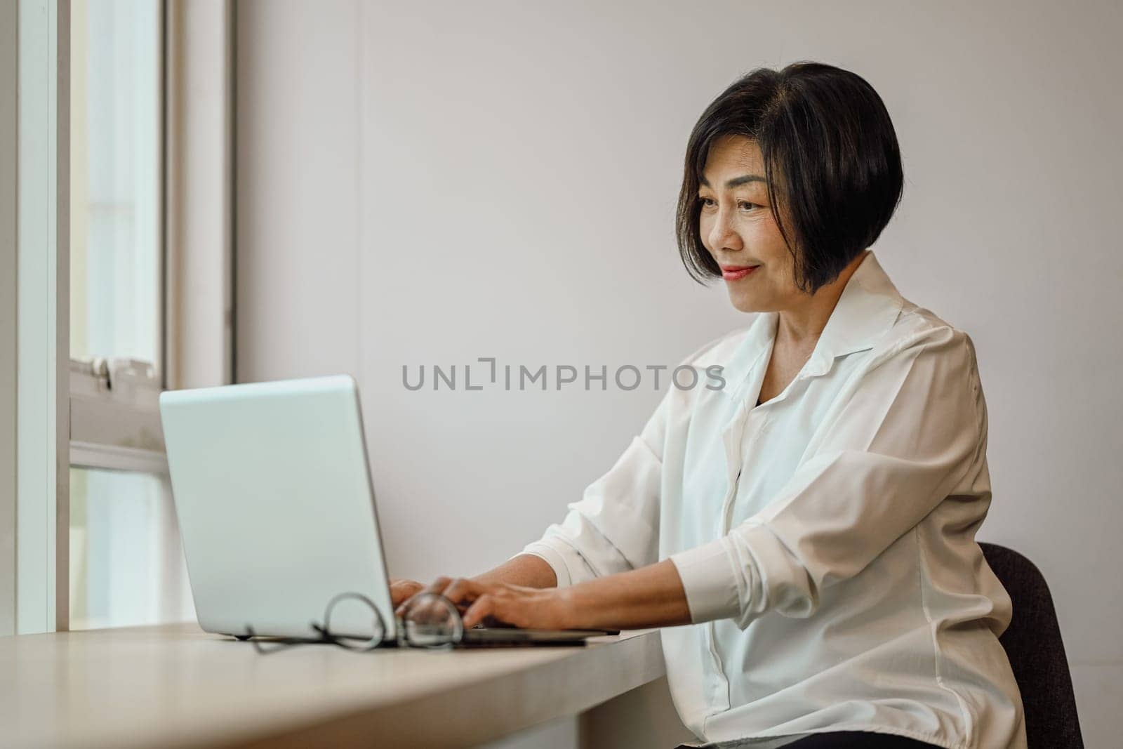 Beautiful senior businesswoman reading email or searching information on laptop at desk.