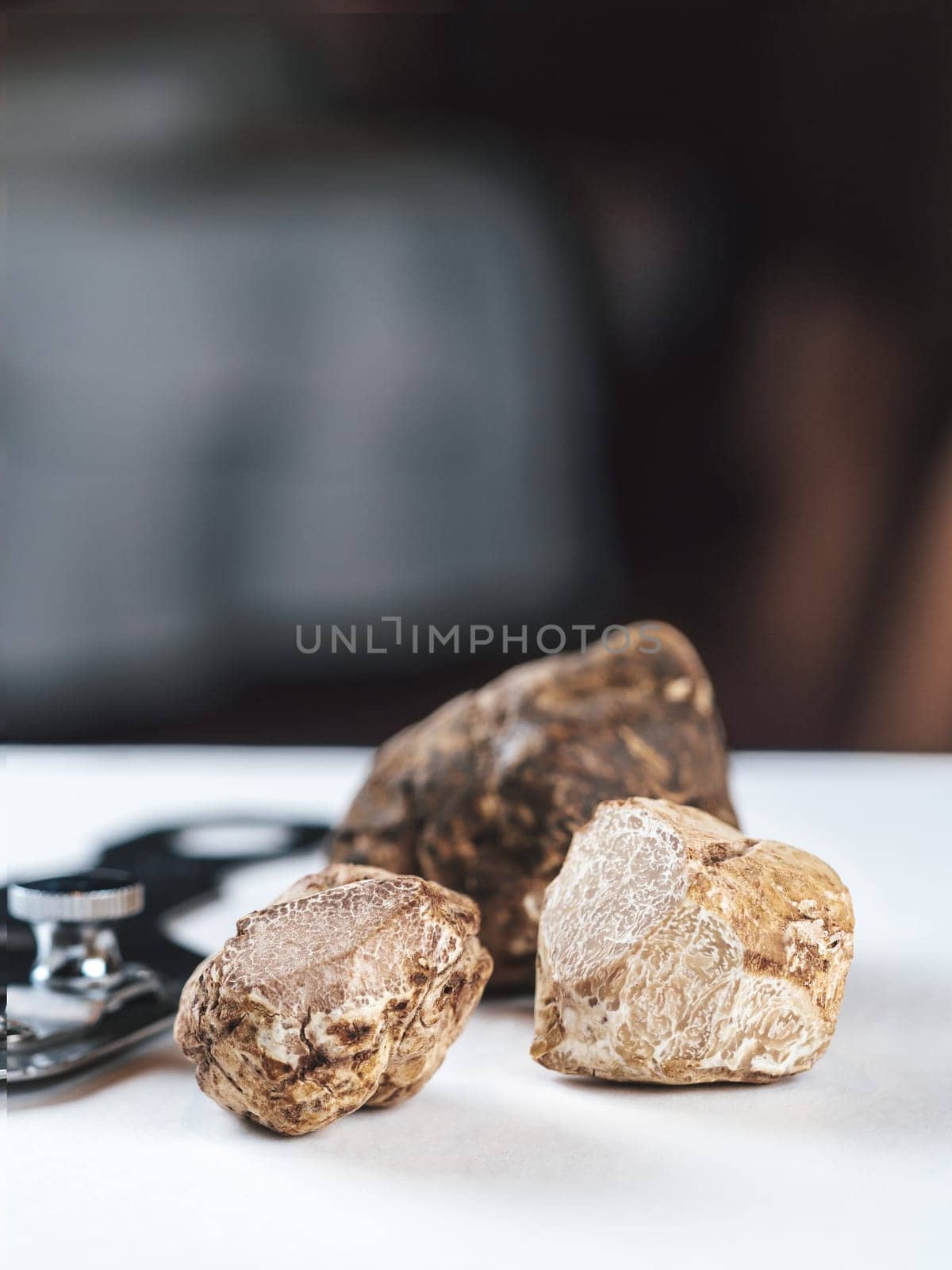 Expensive white truffles gourmet mushrooms on white table in restaurant interior. Row of brown truffles with slice on a white table with dark background. Truffle mushrooms is culinary delight. Close up. Macro.