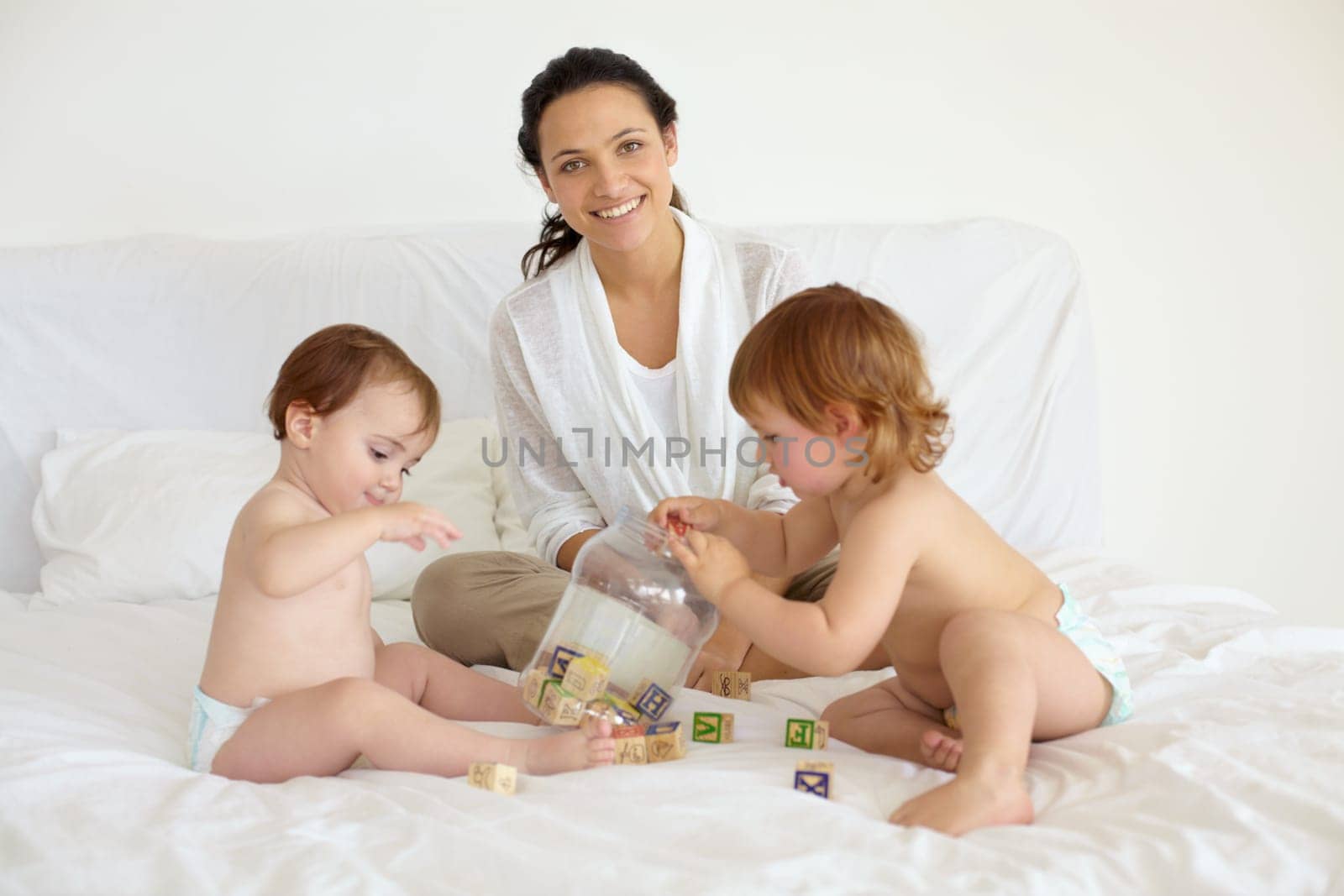 Happy, toys and portrait of mother with babies on the bed playing for child development at home. Smile, love and young mom with wooden building blocks for learning with kids in bedroom at house