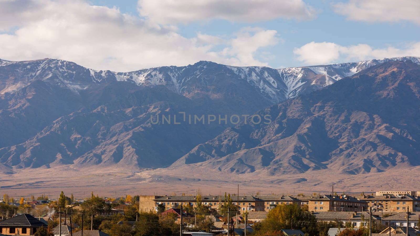 Small Kyrgyz town Balykchy cityscape in front of massive mountain ridge by z1b