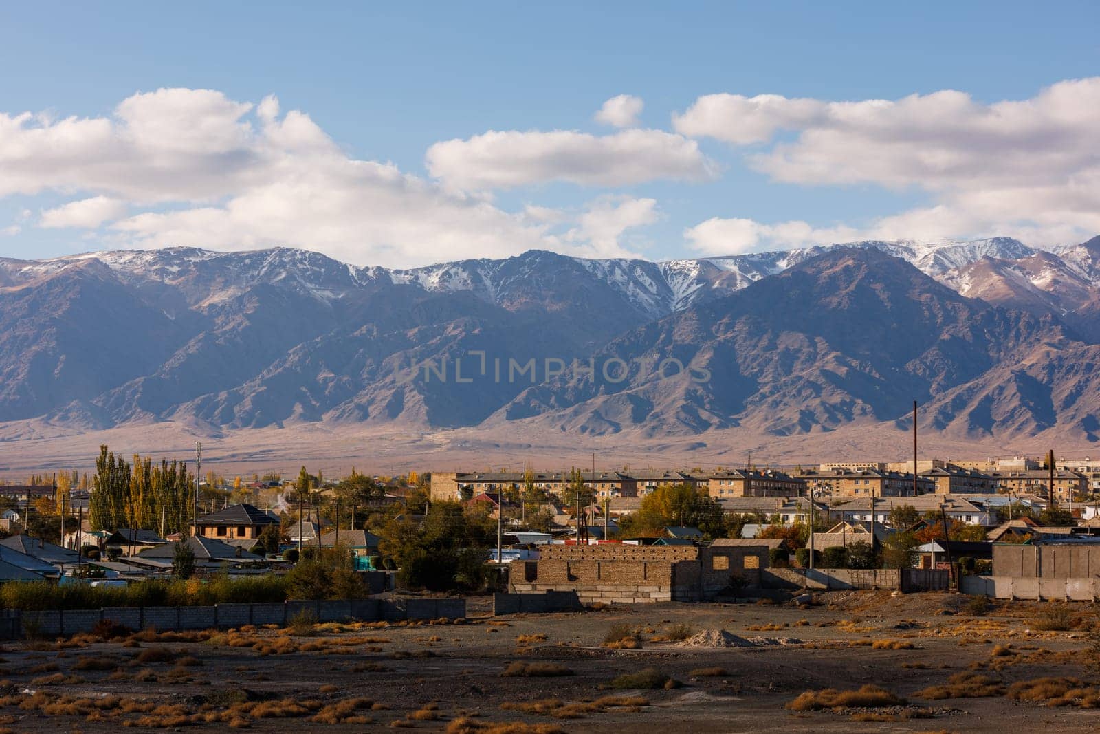 Small Kyrgyz town Balykchy cityscape in front of massive mountain ridge at sunny autumn afternoon