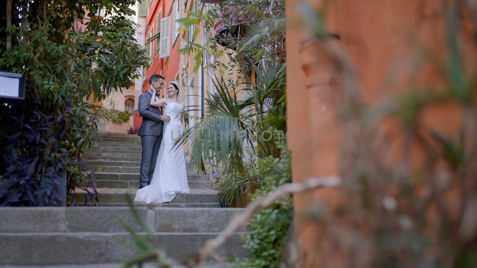 Newlyweds taking pictures on the street. Action. A young couple with a bride in a white dress and a man in a suit who are photographed in full height on the steps next to the architecture of the city. High quality 4k footage