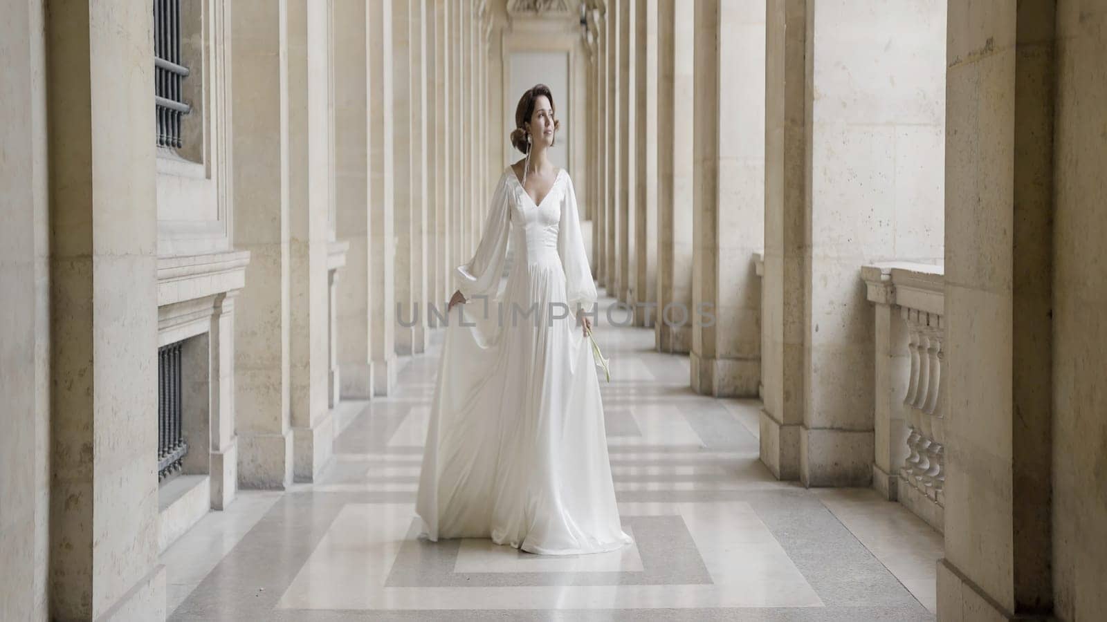 Slim graceful young woman in stylish wedding dress. Action. Sensitive elegant woman in long dress on architectural hall background