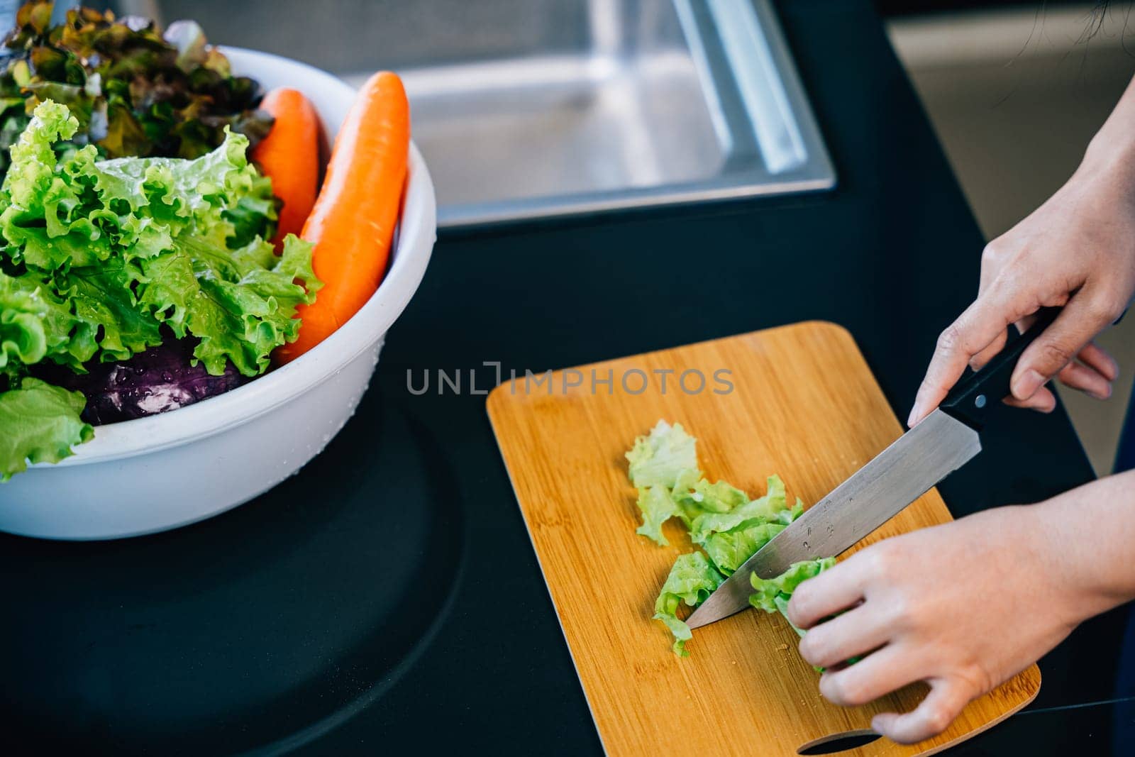 An unrecognizable woman in a blue apron prepares a nutritious dinner cutting vegetables by Sorapop