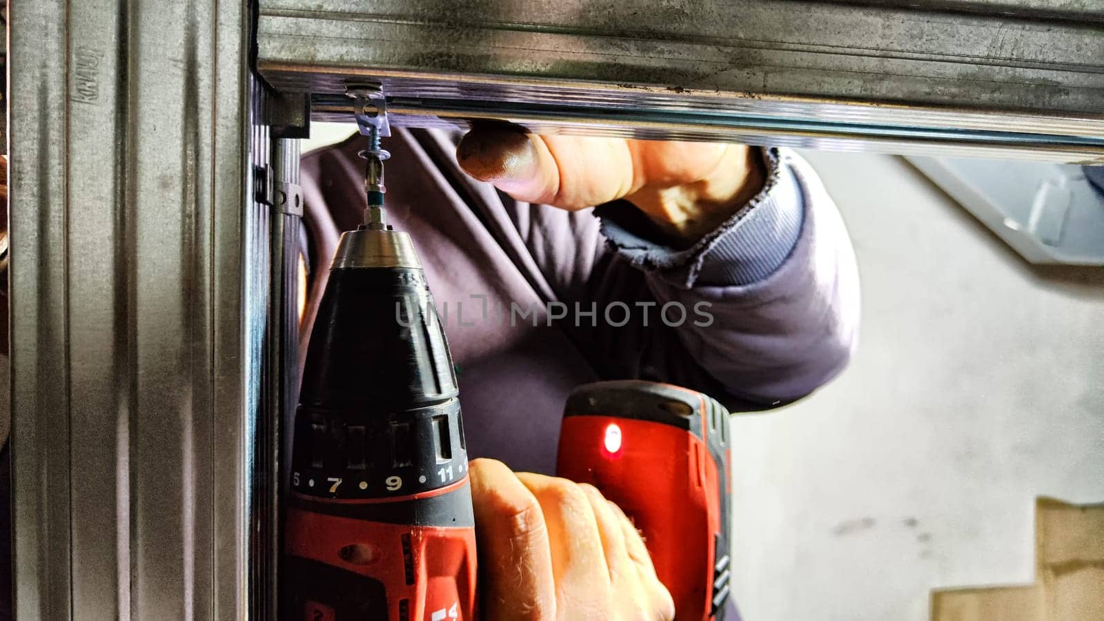 Man hands drilling metal planc in construction. Building iron fence with a drill and screw. Close up of his hand and the tool drill by keleny