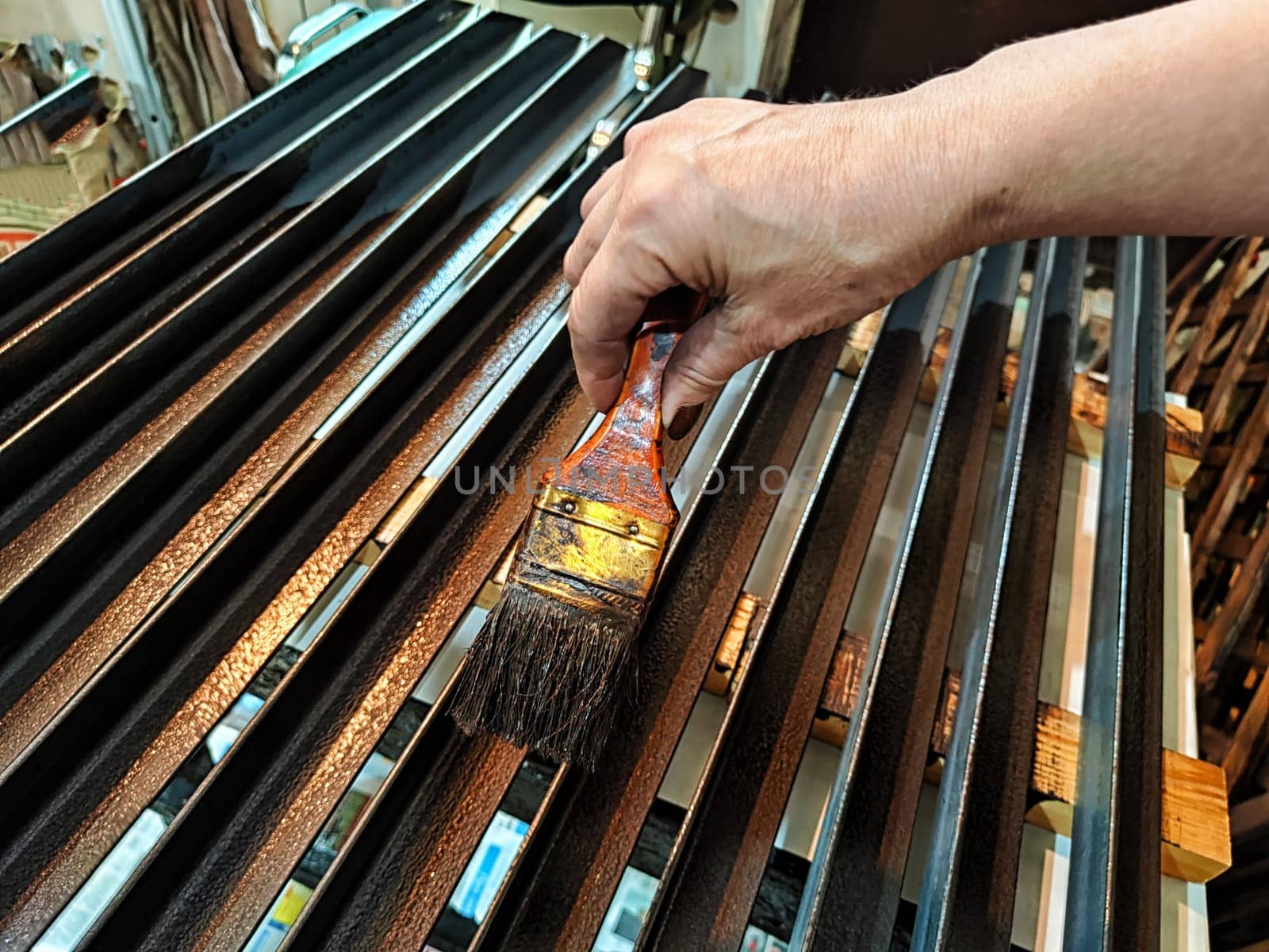 A brush in woman's hand paints iron metal bars with brown paint. Work and worker