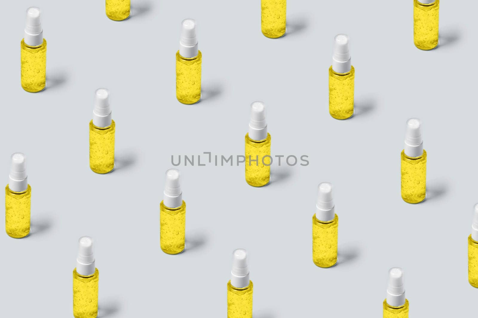 Pattern of bottles with yellow filling on gray background. Advertising cosmetics in the trendy colors of the new year.