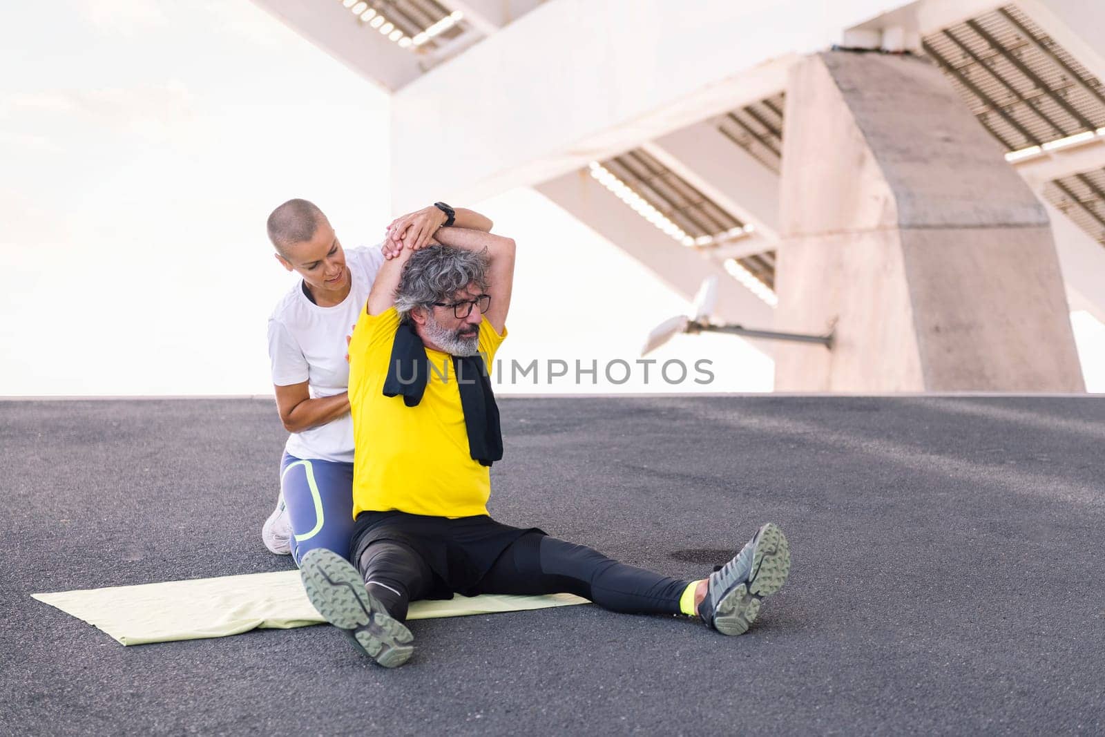 senior sports man stretching arm with assistance of his personal trainer, concept of active and healthy lifestyle in middle age, copy space for text