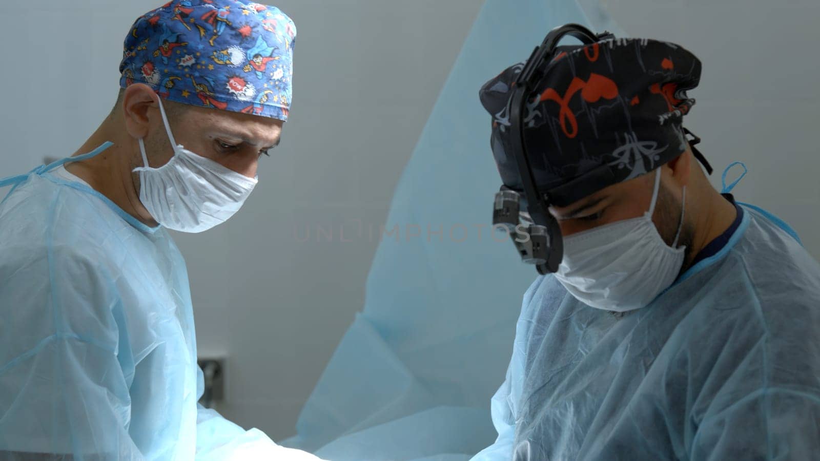 Close up shot of doctor in surgical loupe, sterile mask and protective hair cover looking at the camera. Action. Medical equipment at a hospital