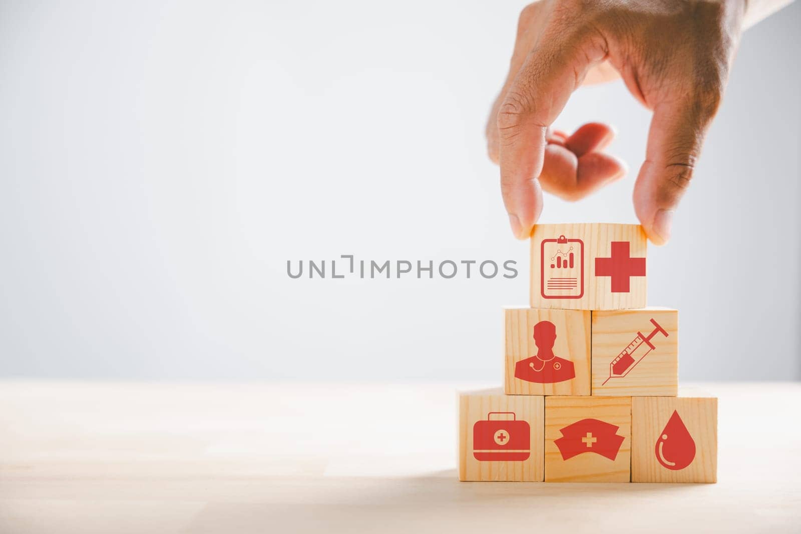 Conceptual portrayal, Hand clutches wooden block with healthcare and medical icons. Reflecting safety, health, and family well-being. Symbolic of pharmacy, heart care, and happiness.