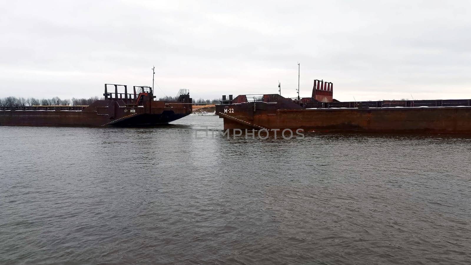Sea transportation with barges. Clip. Floating barges for cargo transportation on river in winter. Barges on river on cloudy winter day.