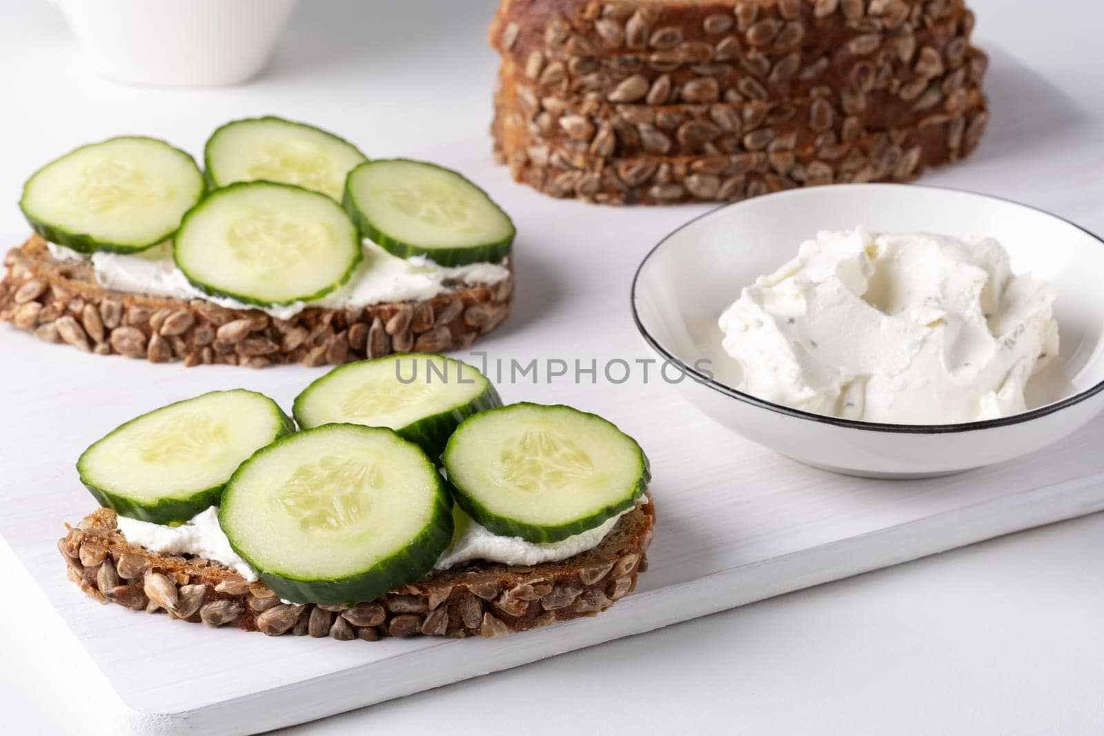 Rye bread with cream cheese and cucumbers on a white table. Whole grain rye bread with seeds.