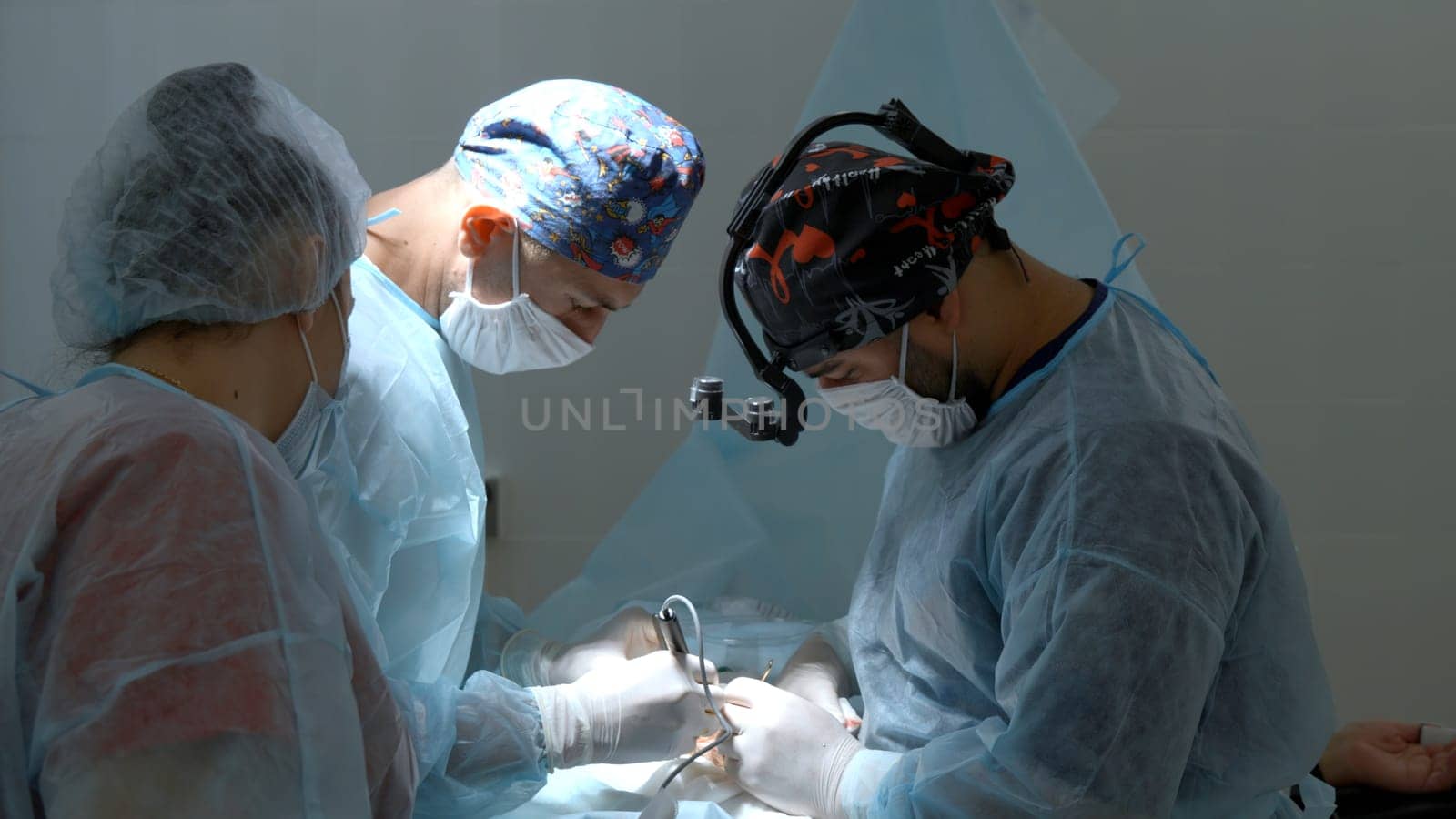 Group of surgeons working in operating room at hospital. Action. Nurse helping two doctors during surgery. by Mediawhalestock