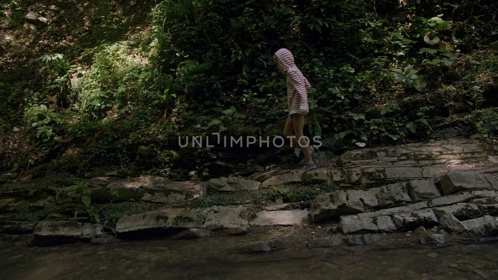 Boy walking in jungles among green forest and mountain river. Creative. Lush green trees and flowing cold river, child exploring wild nature. by Mediawhalestock
