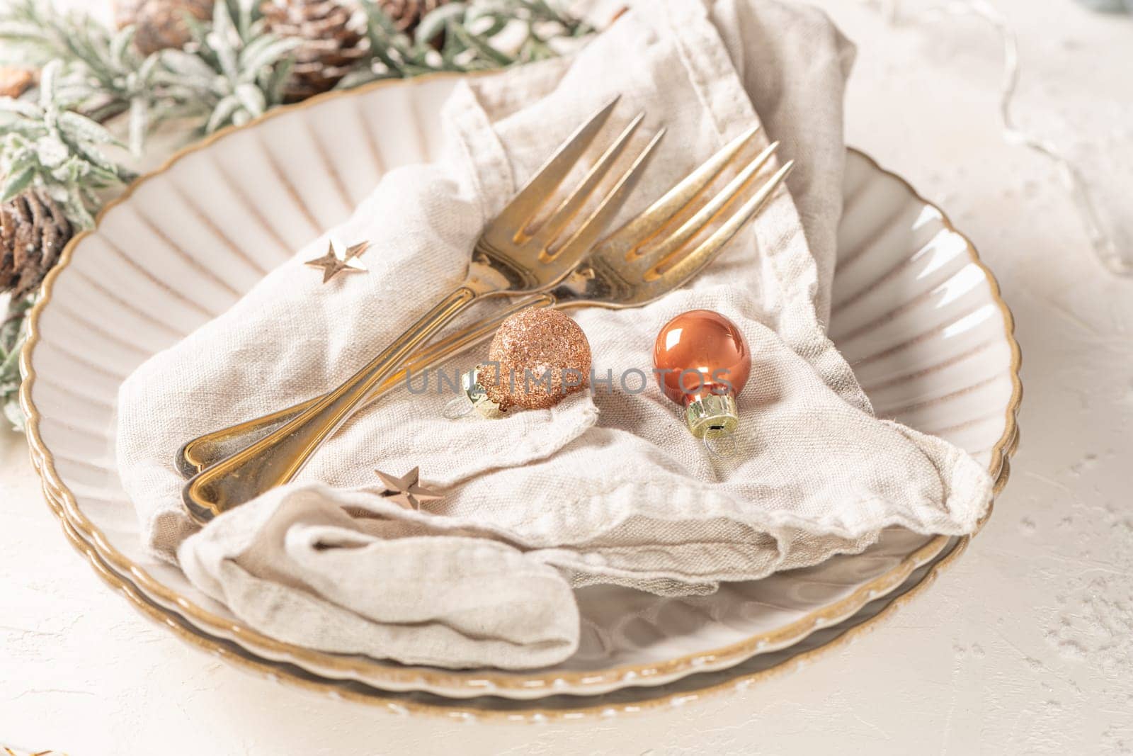 Christmas table with white plates, golden cutlery and holiday decorations.