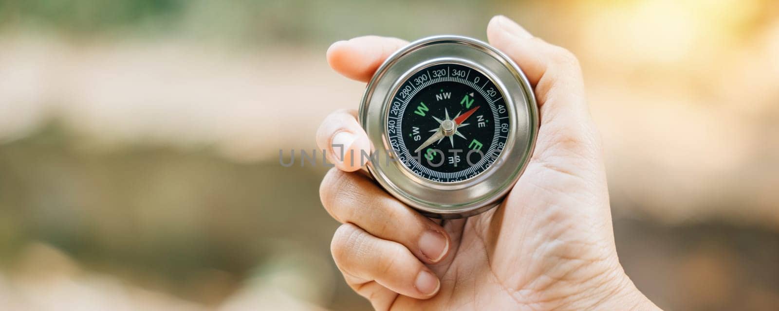 Traveler grasps a compass in park using it to overcome confusion. compass in her hand symbolizes guidance and exploration against nature-blurred backdrop she embarks on journey of discovery in forest. by Sorapop