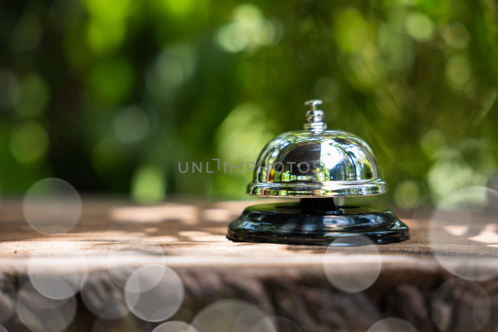Hotel ring bell. Closeup of silver service restaurant bell on wooden counter desk, vintage bell to call staff outdoor in garden with green leaf