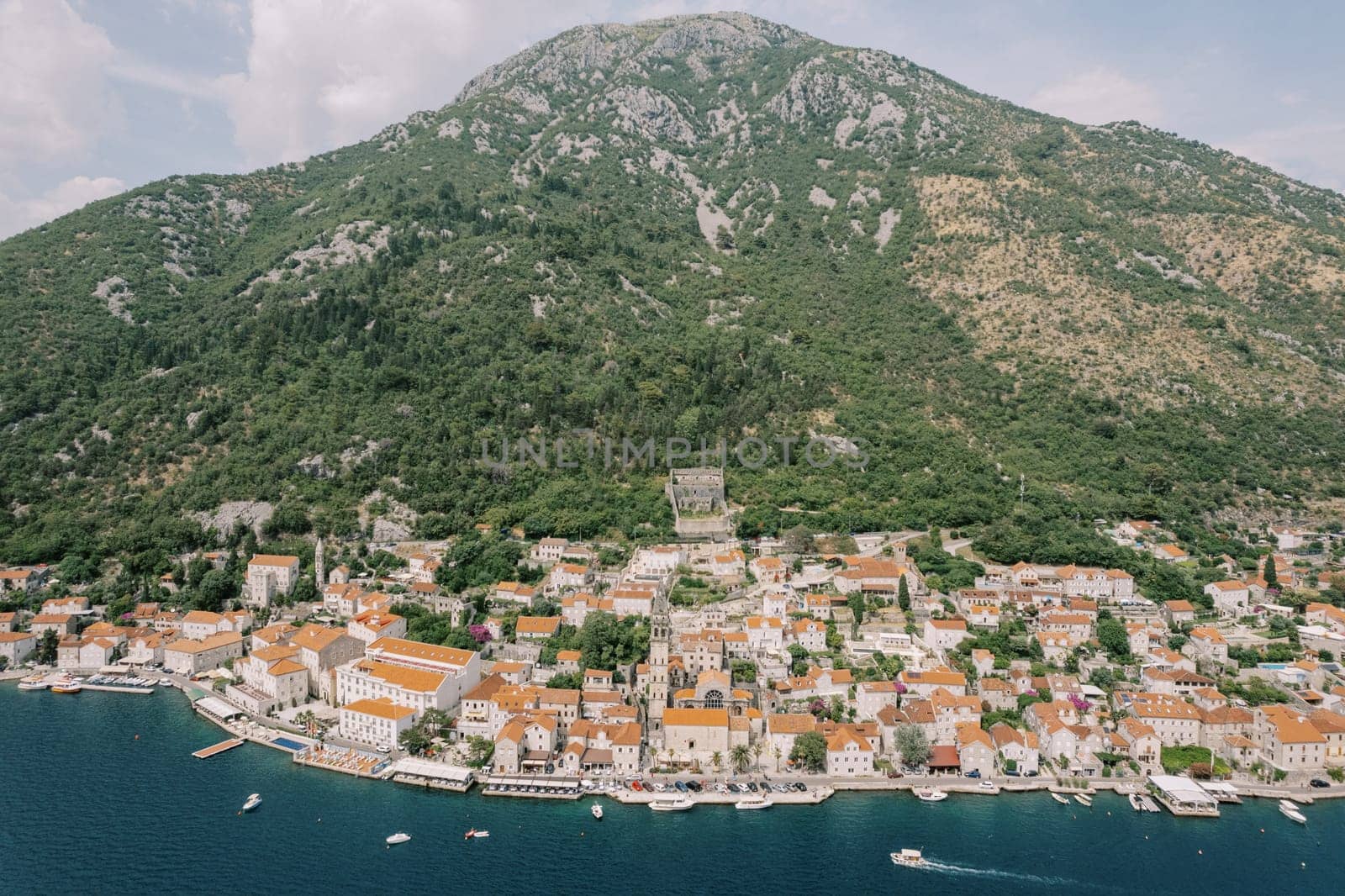 Bell tower of the Church of St. Nicholas among the red roofs of old houses on the shore of the bay. Perast, Montenegro. Drone. High quality photo