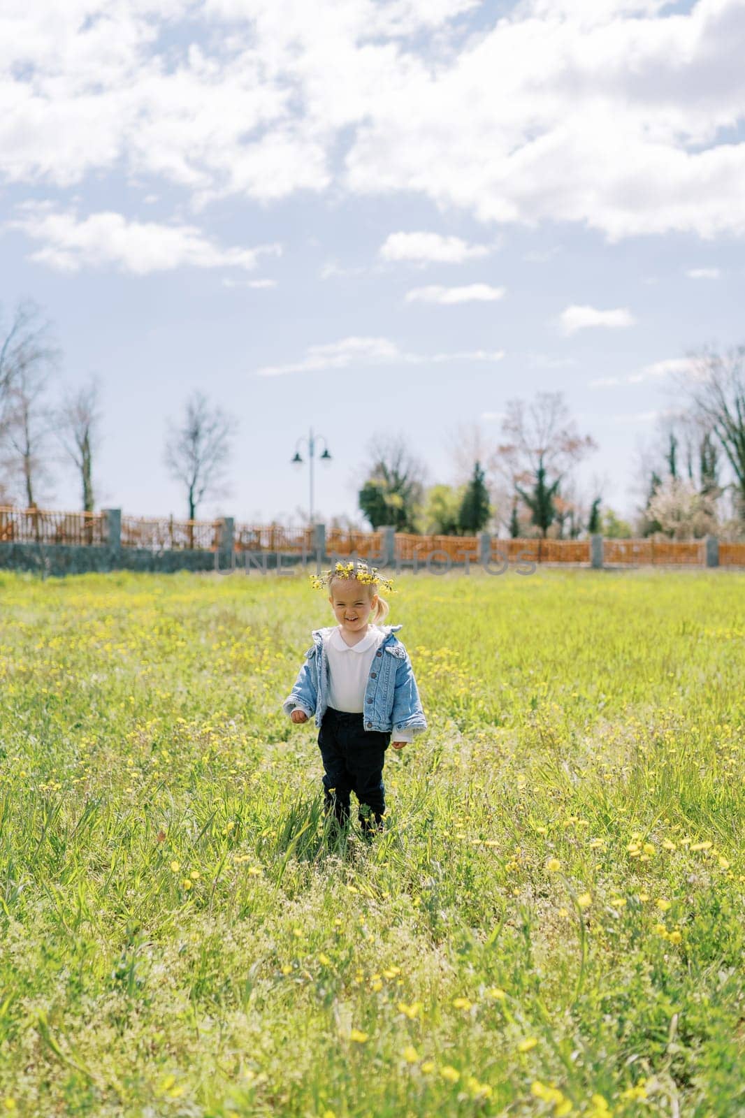 Little smiling girl in a wreath of dandelions stands in a sunny meadow. High quality photo