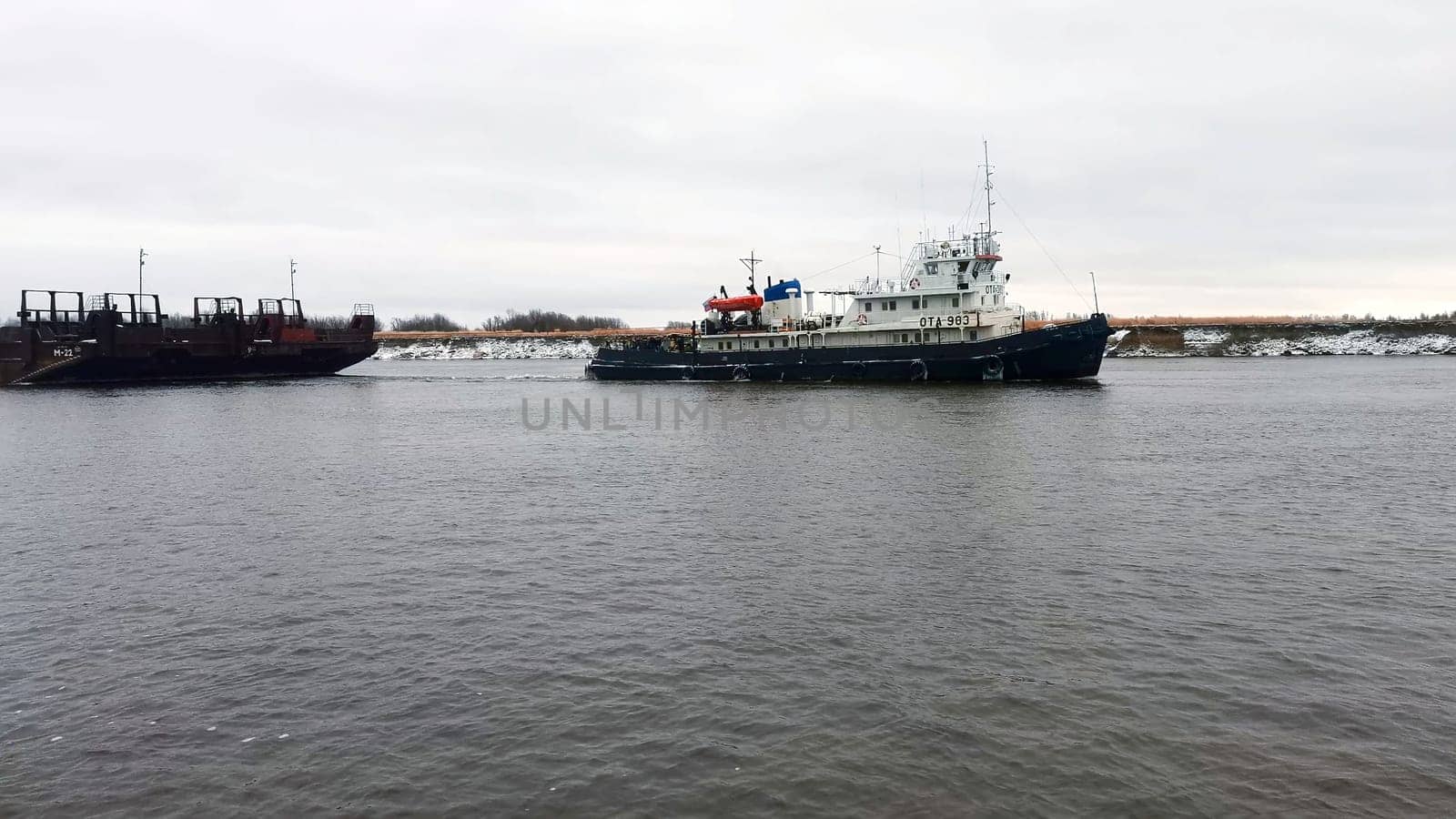 Sea transportation with barges. Clip. Floating barges for cargo transportation on river in winter. Barges on river on cloudy winter day by Mediawhalestock