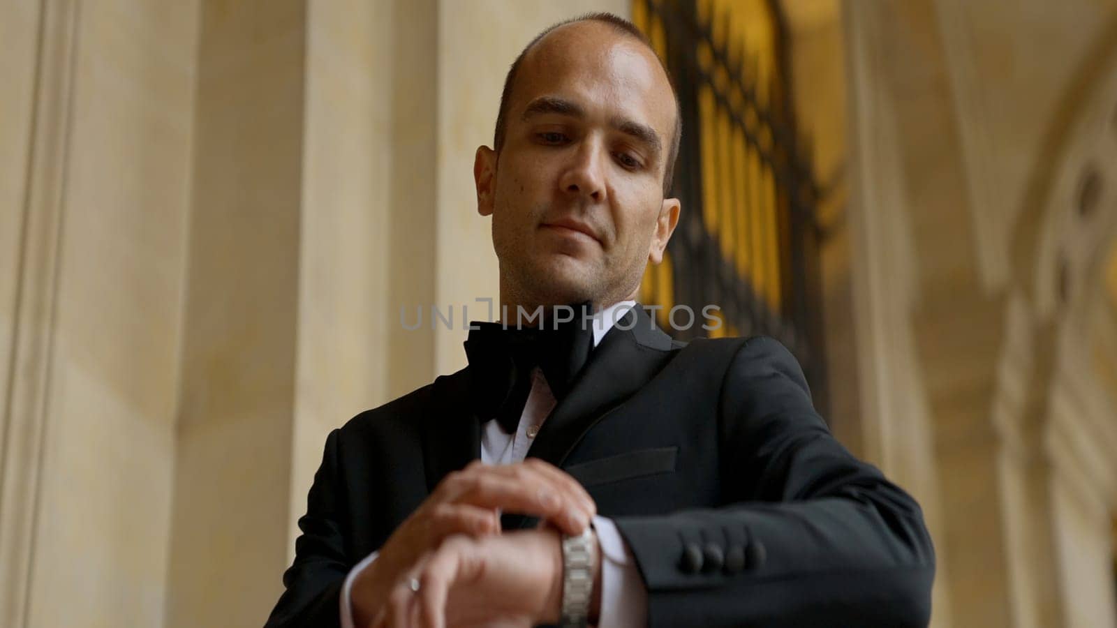 Low angle view of a man looking at his watch on the background of an ancient building. Action. Elegant man in suit. by Mediawhalestock