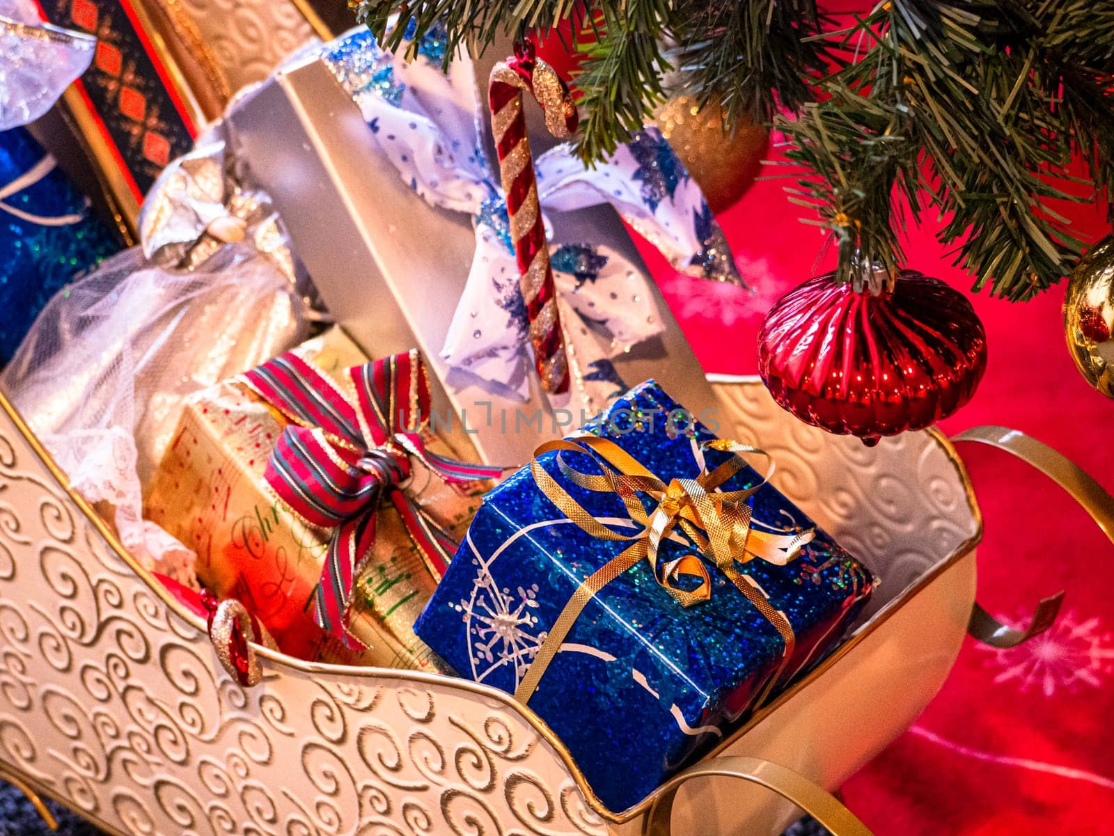 Decorative Santa Claus sleigh with coloured gifts boxes on red carpet under Christmas tree