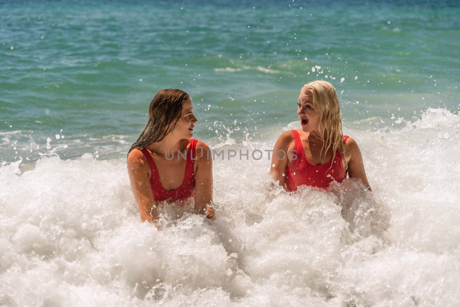 Women ocean play. Seaside, beach daytime, enjoying beach fun. Two women in red swimsuits enjoying themselves in the ocean waves. by Matiunina