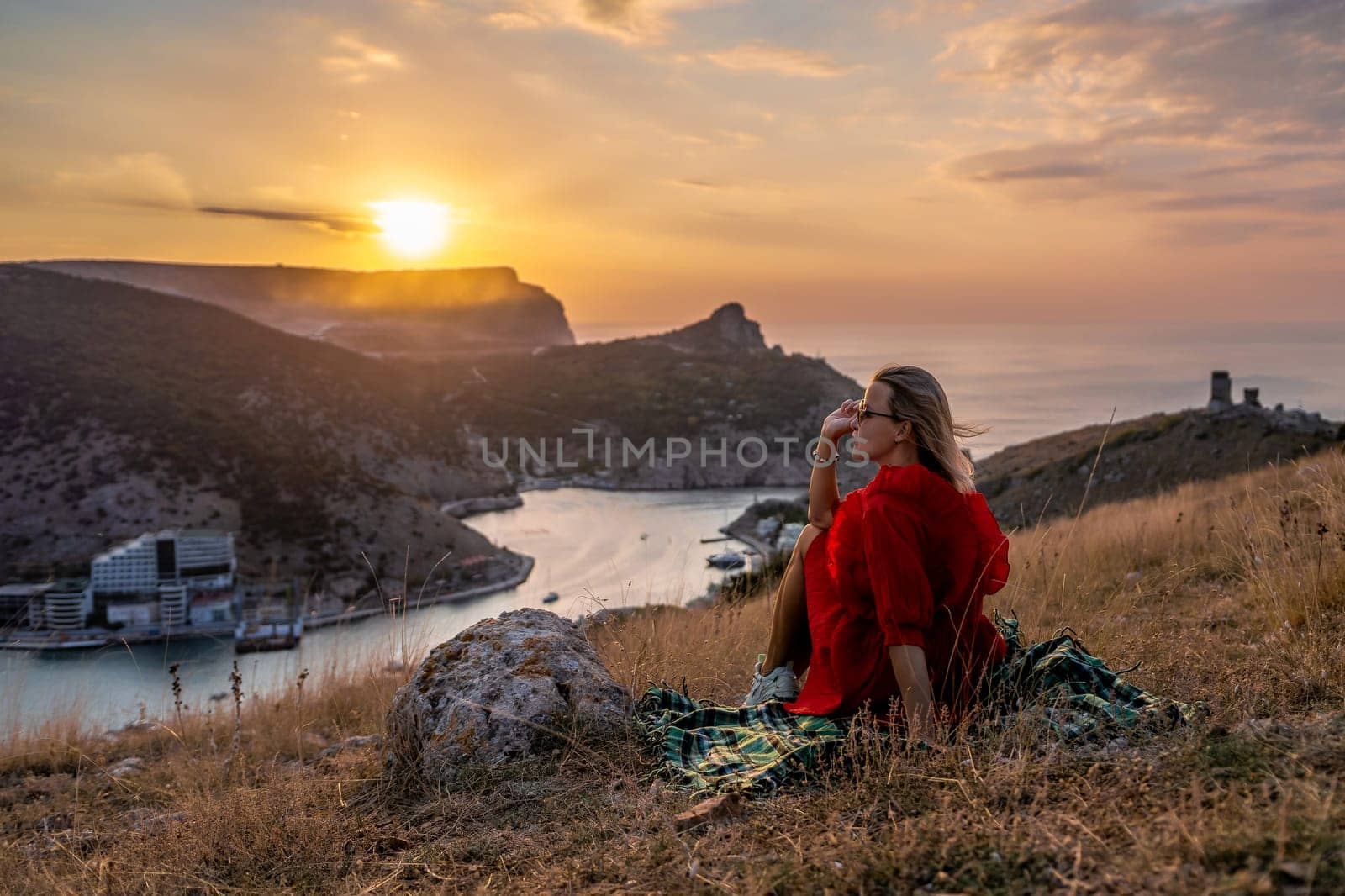 Woman sunset sea mountains. Happy woman siting with her back on the sunset in nature summer posing with mountains on sunset, silhouette. Woman in the mountains red dress, eco friendly, summer landscape active rest.