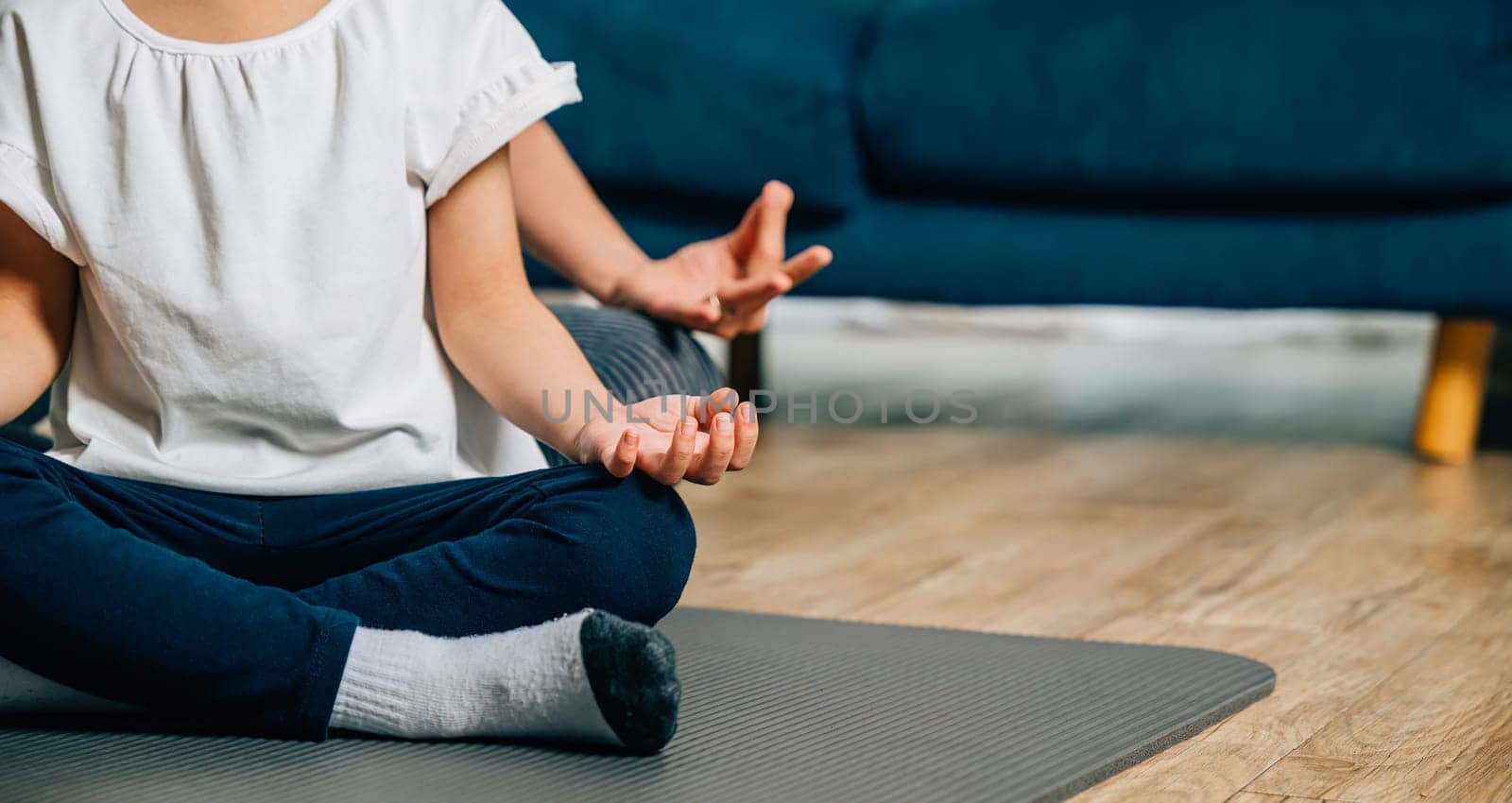 A mother and her daughter find joy in family yoga sitting in lotus position and focusing on mindfulness and meditation creating a harmonious and joyful family moment at home.