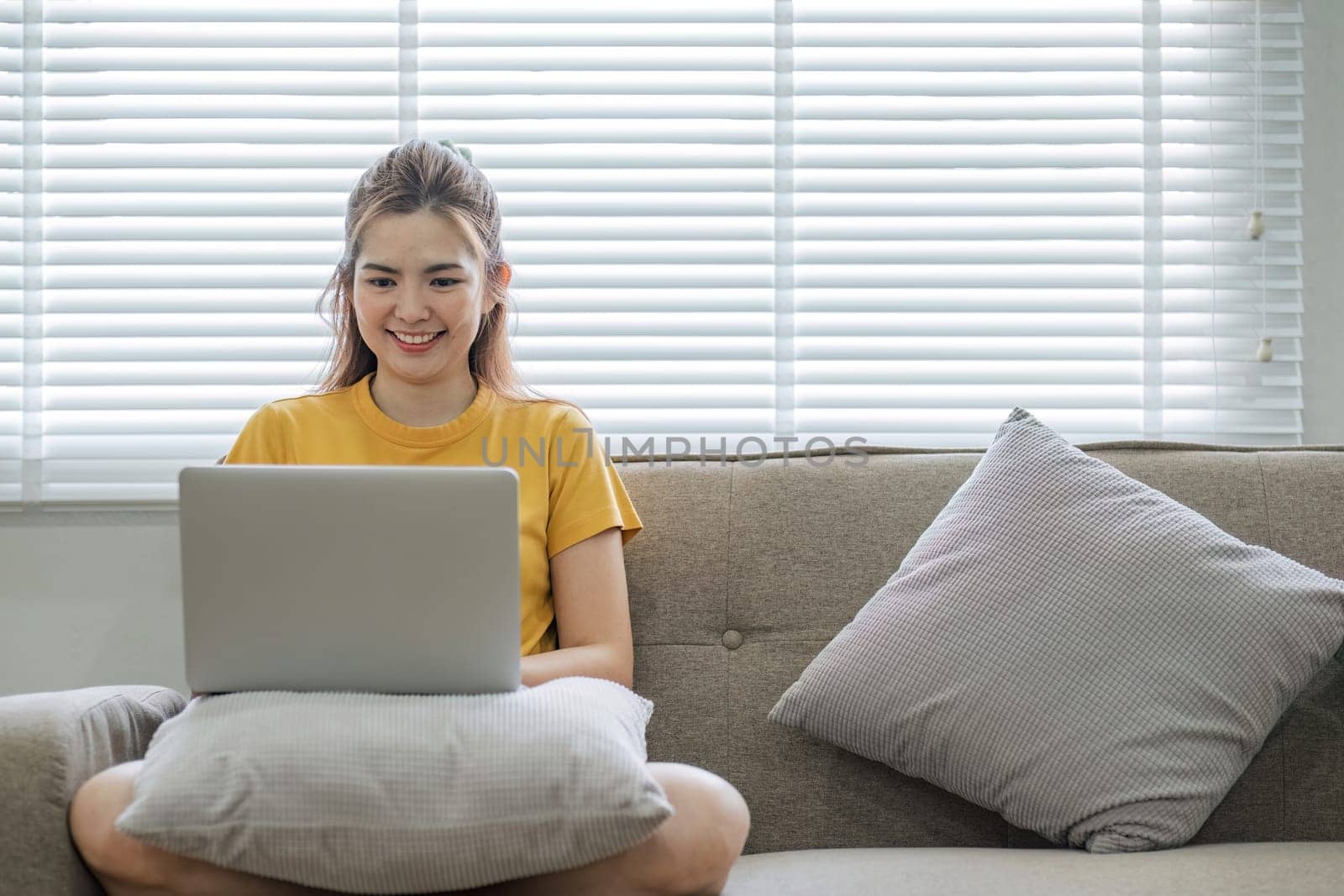 Beautiful Asian woman wearing casual clothes On the sofa using a laptop computer, entertaining with social media, relaxing, smiling and laughing..