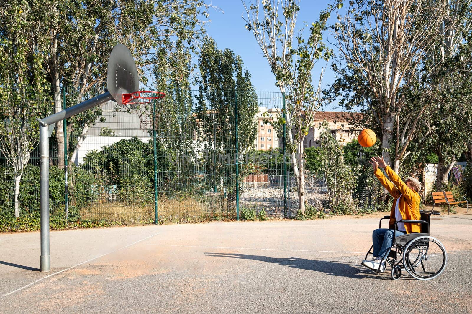Side view of African American man in a wheelchair throwing basketball in court. by Hoverstock