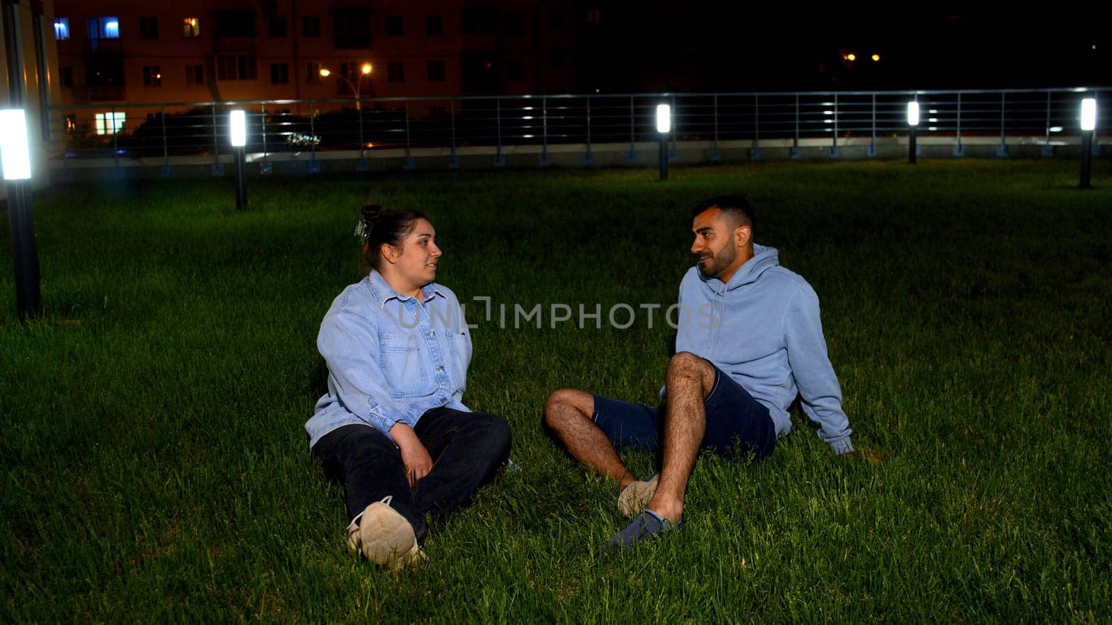 A man and a woman on a lawn in a city park looking happy while talking. Media. The concept of a family weekend and walks in the park