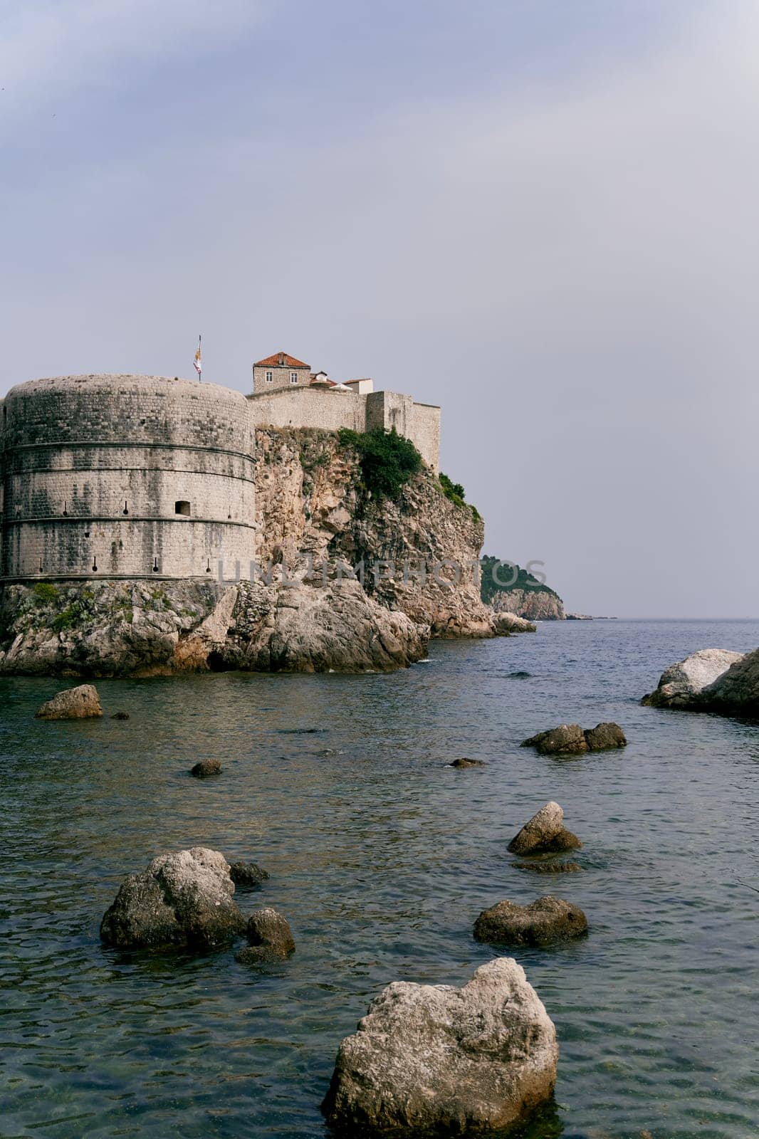 Large boulders peek out of the sea near Bokar Fortress. Dubrovnik, Croatia by Nadtochiy