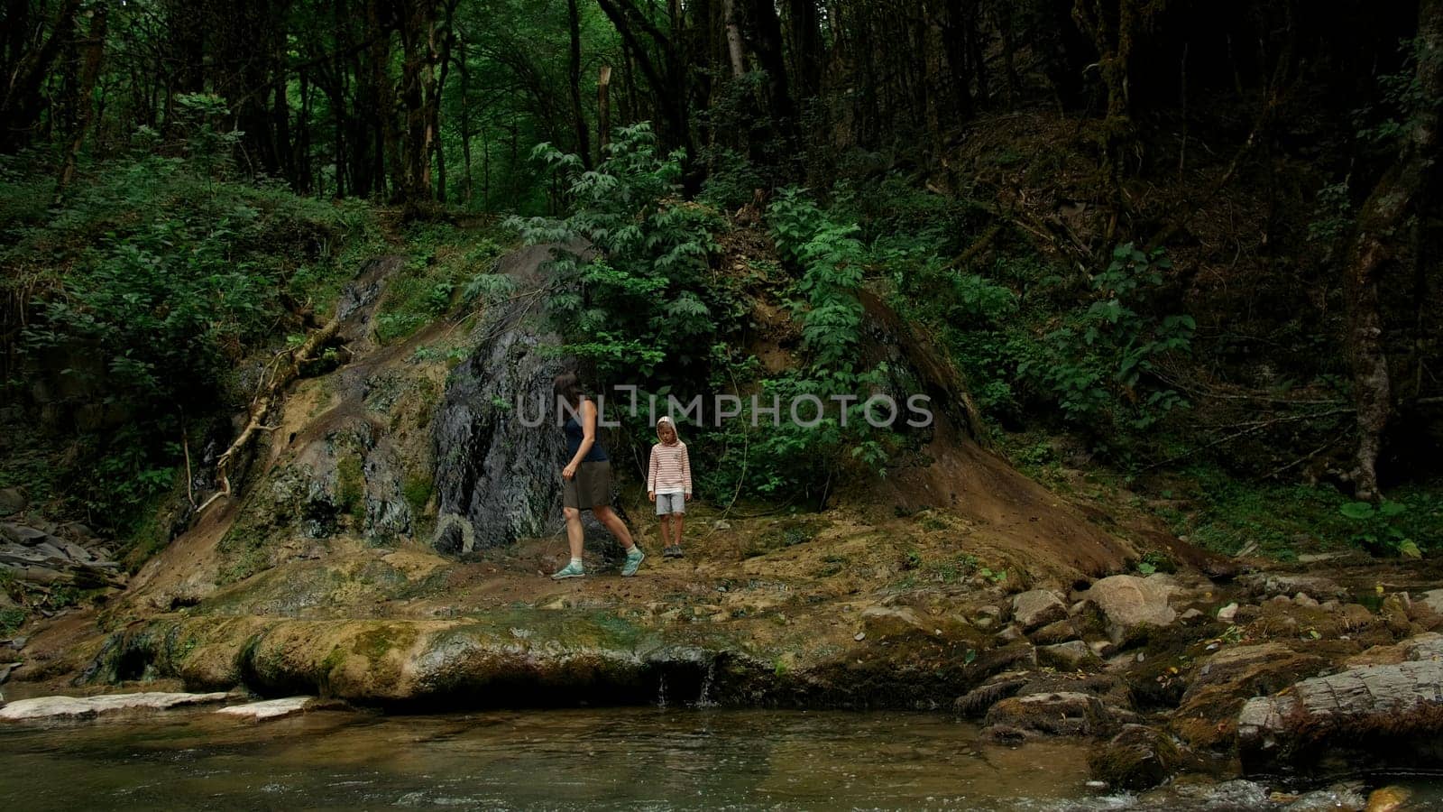 Mother and boy walking along the river and giant stones. Creative. Green dense forest on the background