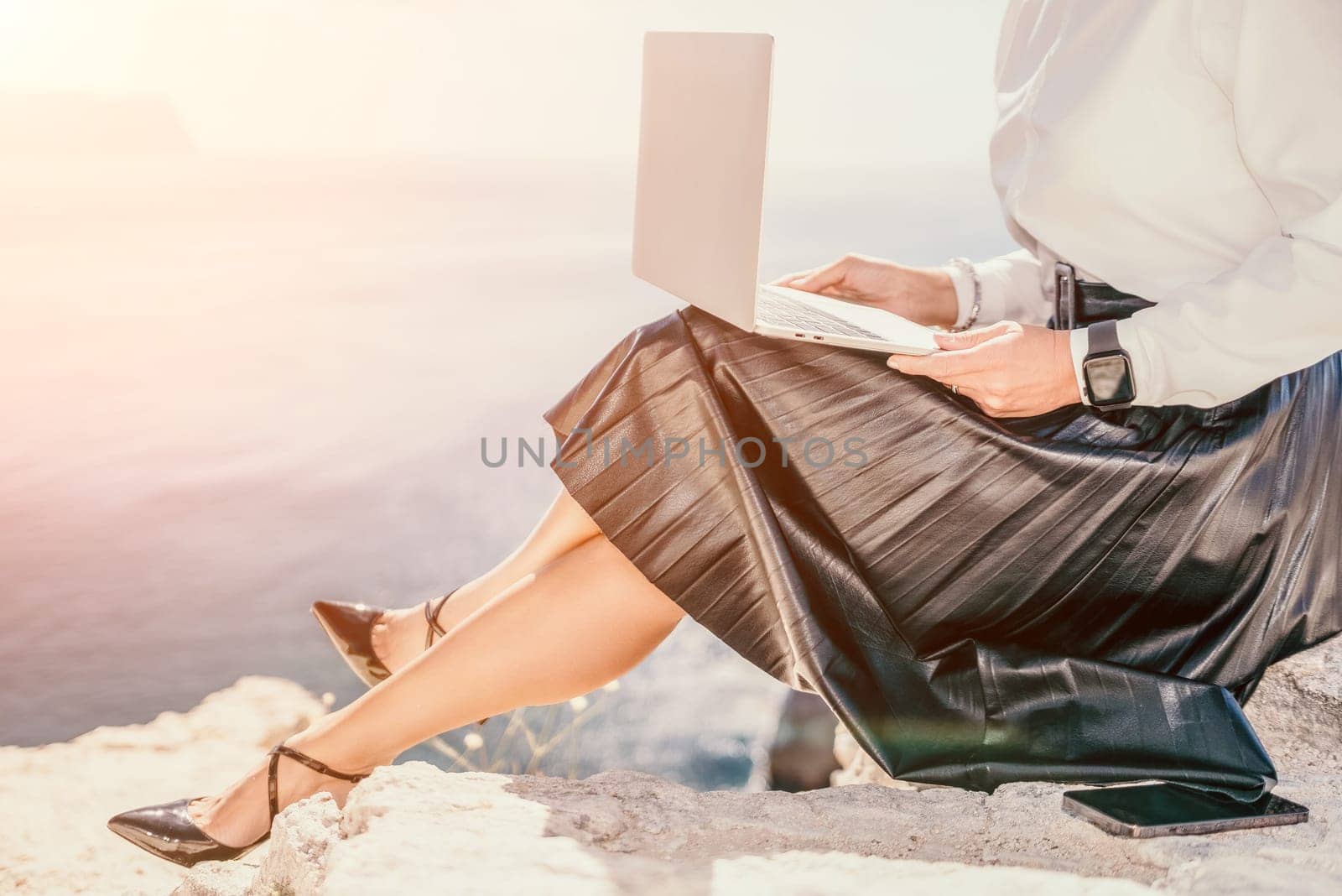 Digital nomad, Business woman working on laptop by the sea. Pretty lady typing on computer by the sea at sunset, makes a business transaction online from a distance. Freelance, remote work on vacation